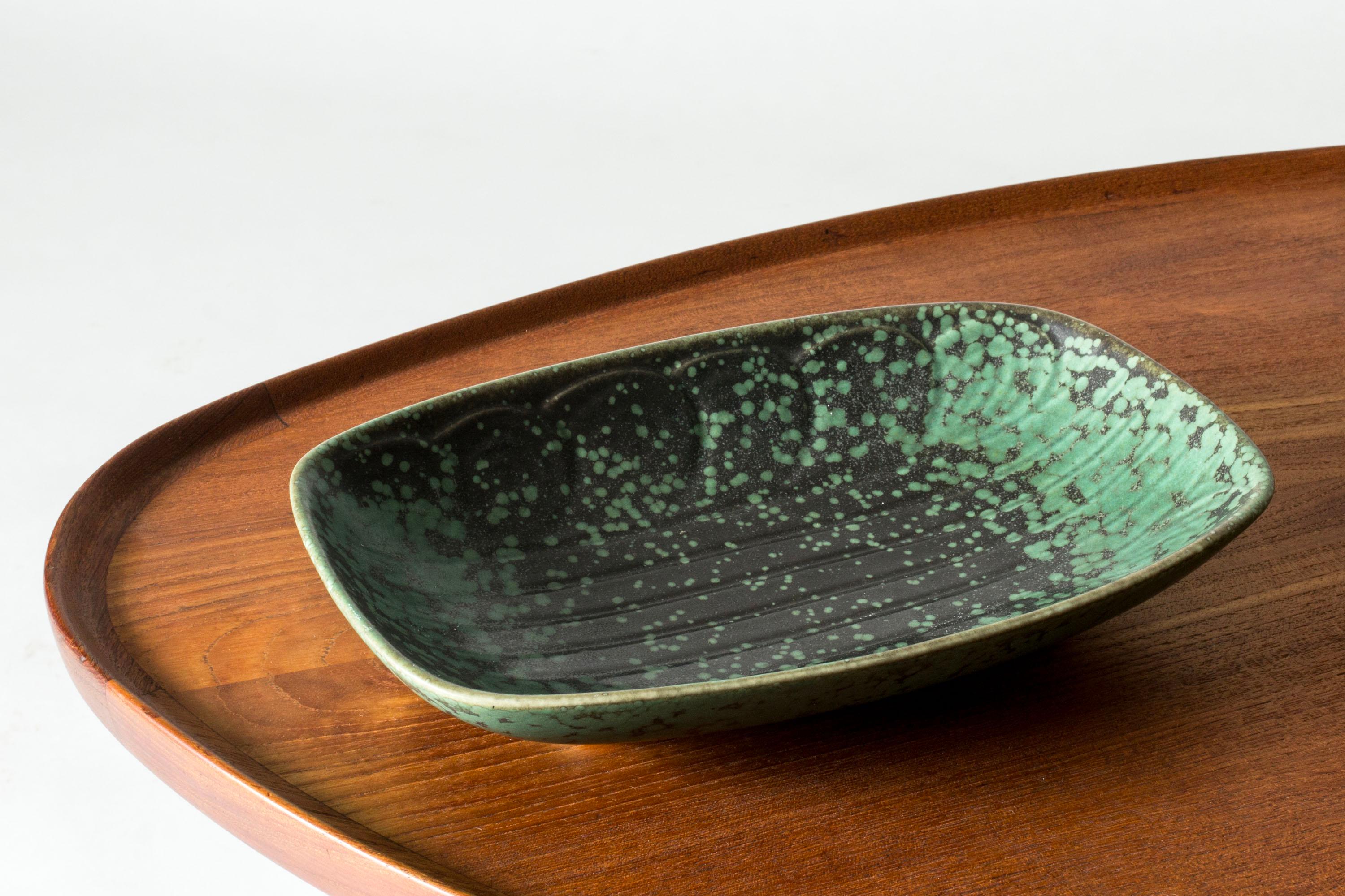 Beautiful stoneware platter by Gunnar Nylund, with an embossed pattern. Dark brown glaze with celadon green “Mimosa” flecks.

Gunnar Nylund was one of the most influential ceramicists and designers of the Swedish mid-century period. He was