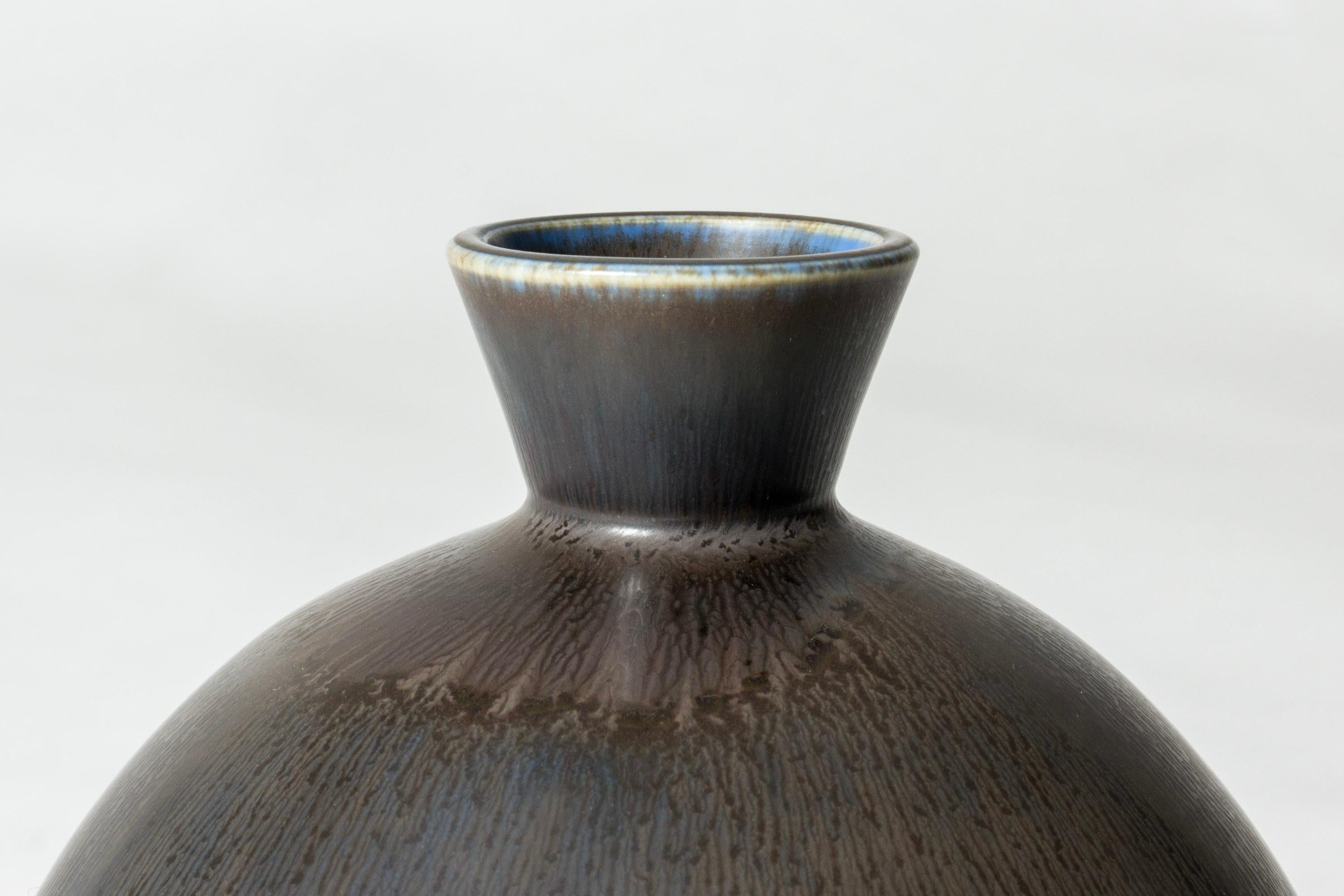 Vaso rotondo in gres di Berndt Friberg, dal collo compatto. Smalto a pelo di lepre grigio bruno con blu alla base e sul bordo.

Berndt Friberg era un ceramista svedese, famoso per i suoi vasi e recipienti in gres per Gustavsberg. I suoi disegni puri