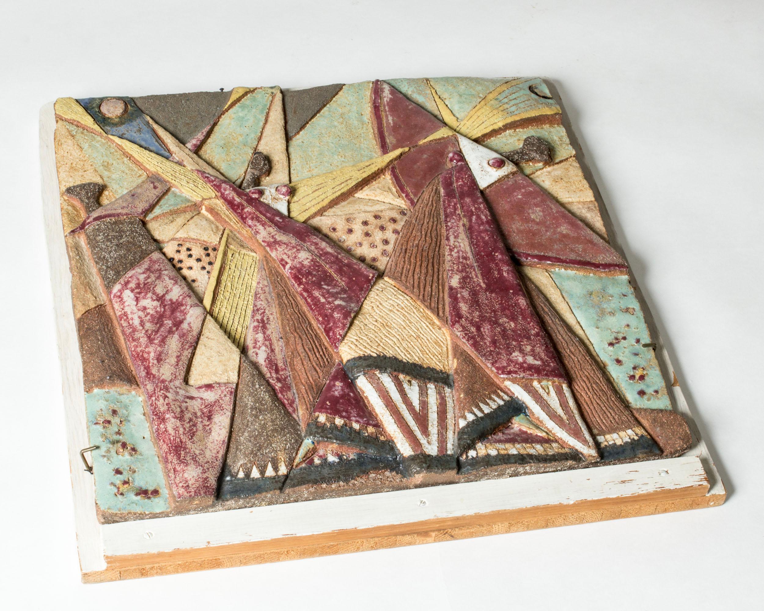 Striking stoneware wall relief by Tyra Lundgren, with a colorful, abstract motif of three dancing women. Beautiful colors and and thick glazes on tactile chamotte.

Mounted on a wooden board. The stoneware piece itself has the following