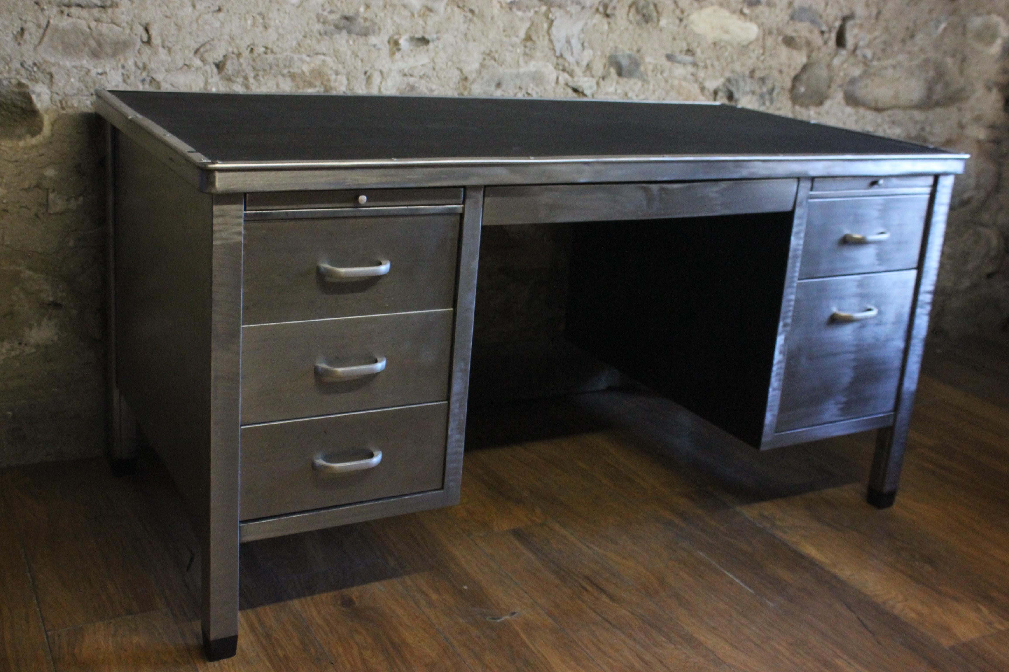 A handsome vintage English stripped metal tanker desk from the 1950s. It has three drawers on one side, two drawers on the other, a centre drawer and two pull out shelves which all run smoothly. It has its original top and has been stripped back to