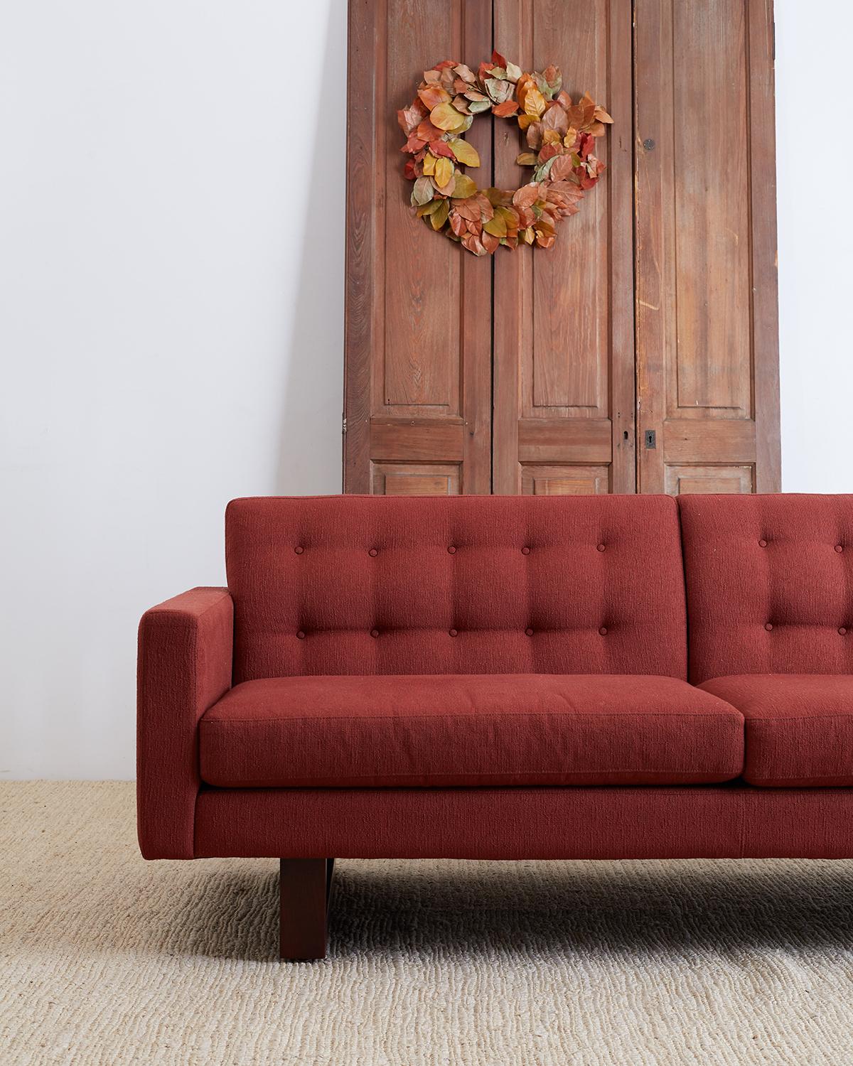 Midcentury style sofa by Room and Board featuring a festive cranberry upholstery. Made in the style of a case sofa with two deep cushion seat pads and a tufted back. Clean modern style with wooden cube shaped legs to complement the design. Very good