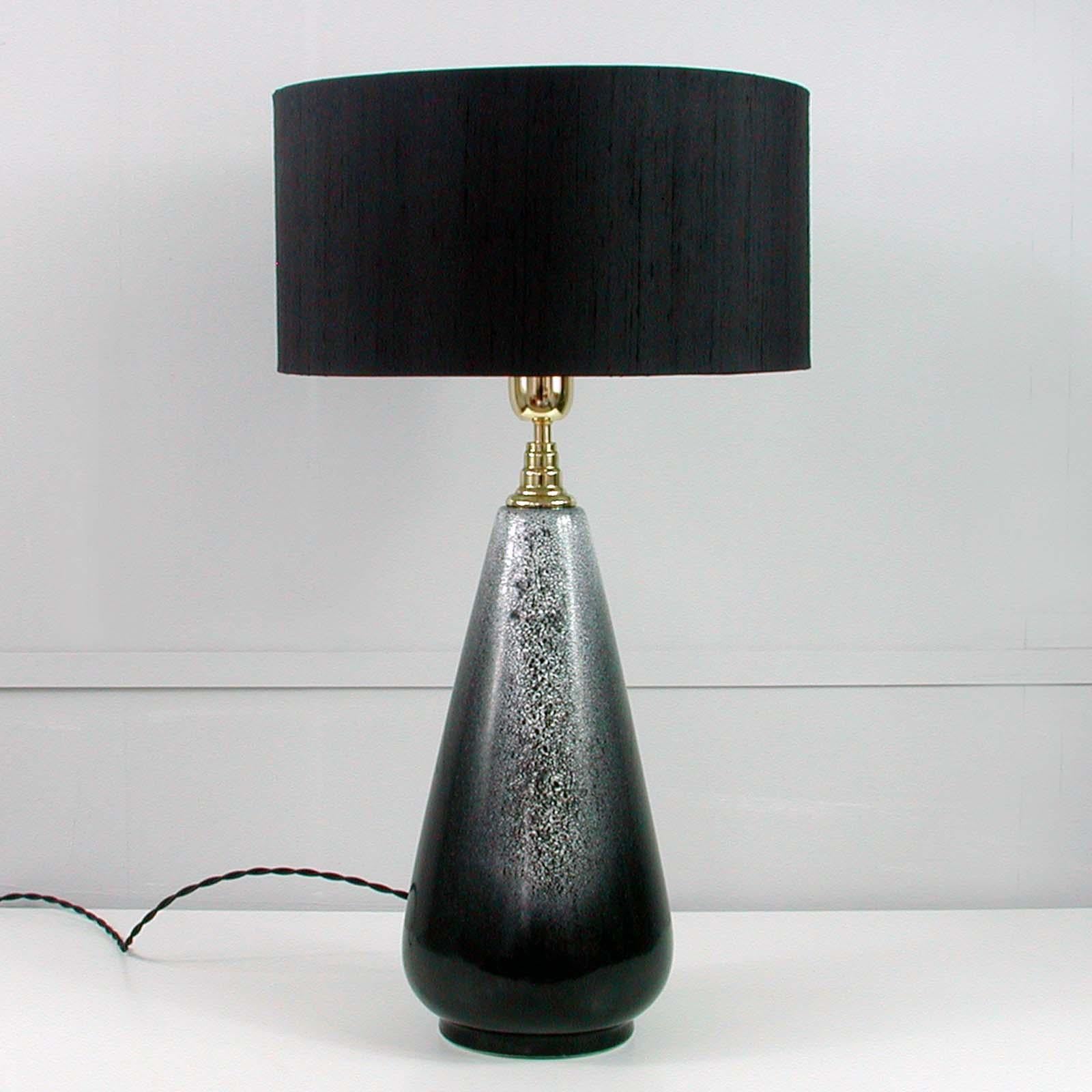 This very large and elegant Scandinavian Modern table lamp was designed and manufactured in Sweden in the 1960s. It has got a black / grey / white ceramic base and a brass bulb holder.  

The lamp has been rewired (with black silk cord) and