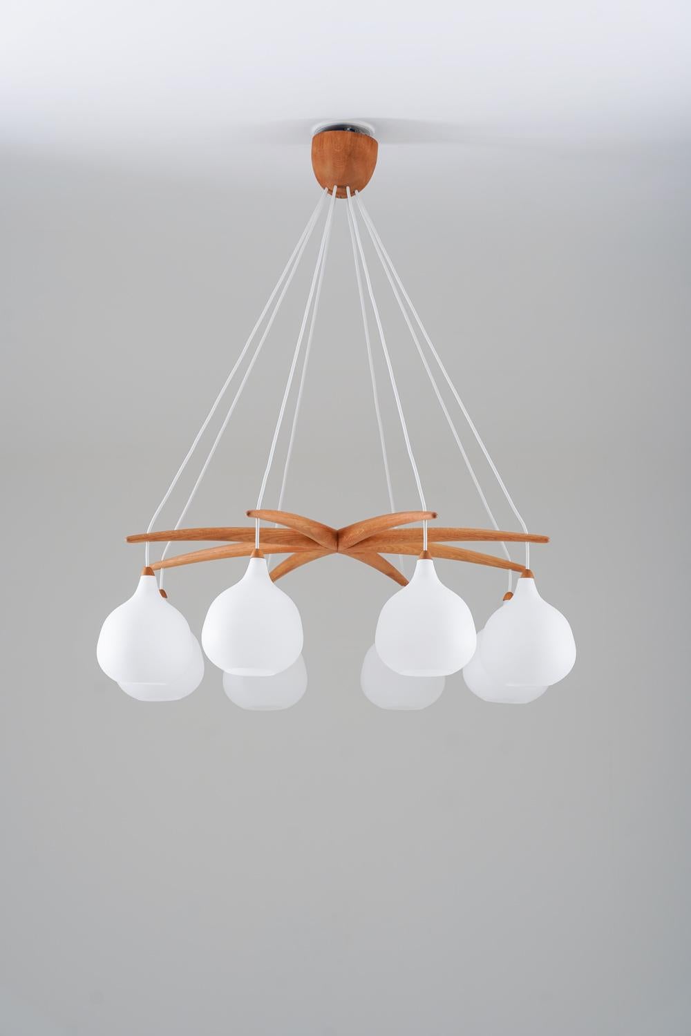 Rare chandelier by Uno & Östen Kristiansson for Luxus, Sweden.

An elegant and sculptural ceiling light by Luxus, Sweden, dating from the 1960s. Eight opaline glass shades are suspended from delicately curved teak arms, all converging into a refined