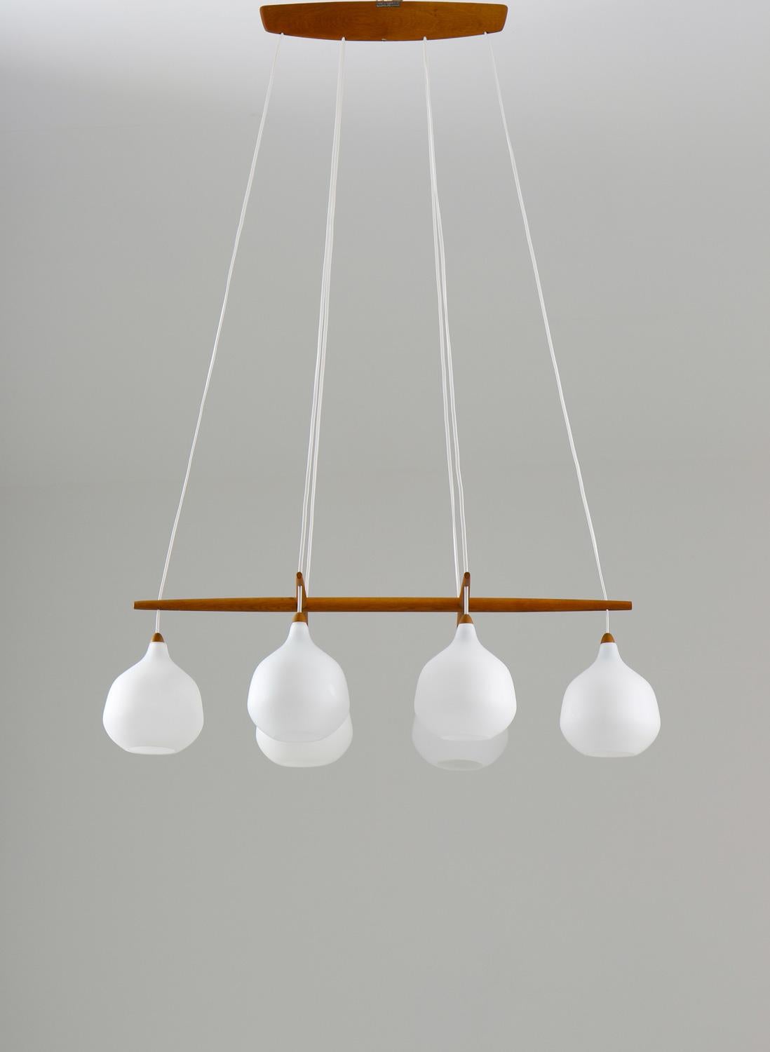 Very rare chandelier model 556 by Uno & Östen Kristiansson for Luxus, Sweden.
The chandelier features six opaline glass globes, separated by an elegant divider in teak, which can be moved to adjust the height of the globes. The frosted opaline