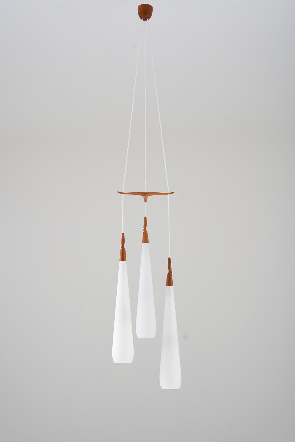 Chandelier by Uno & Östen Kristiansson for Luxus, Sweden.
The chandelier features three large opaline glass shades, separated by an elegant divider in teak, which can be moved to adjust the height of the shades. The frosted opaline glass gives a