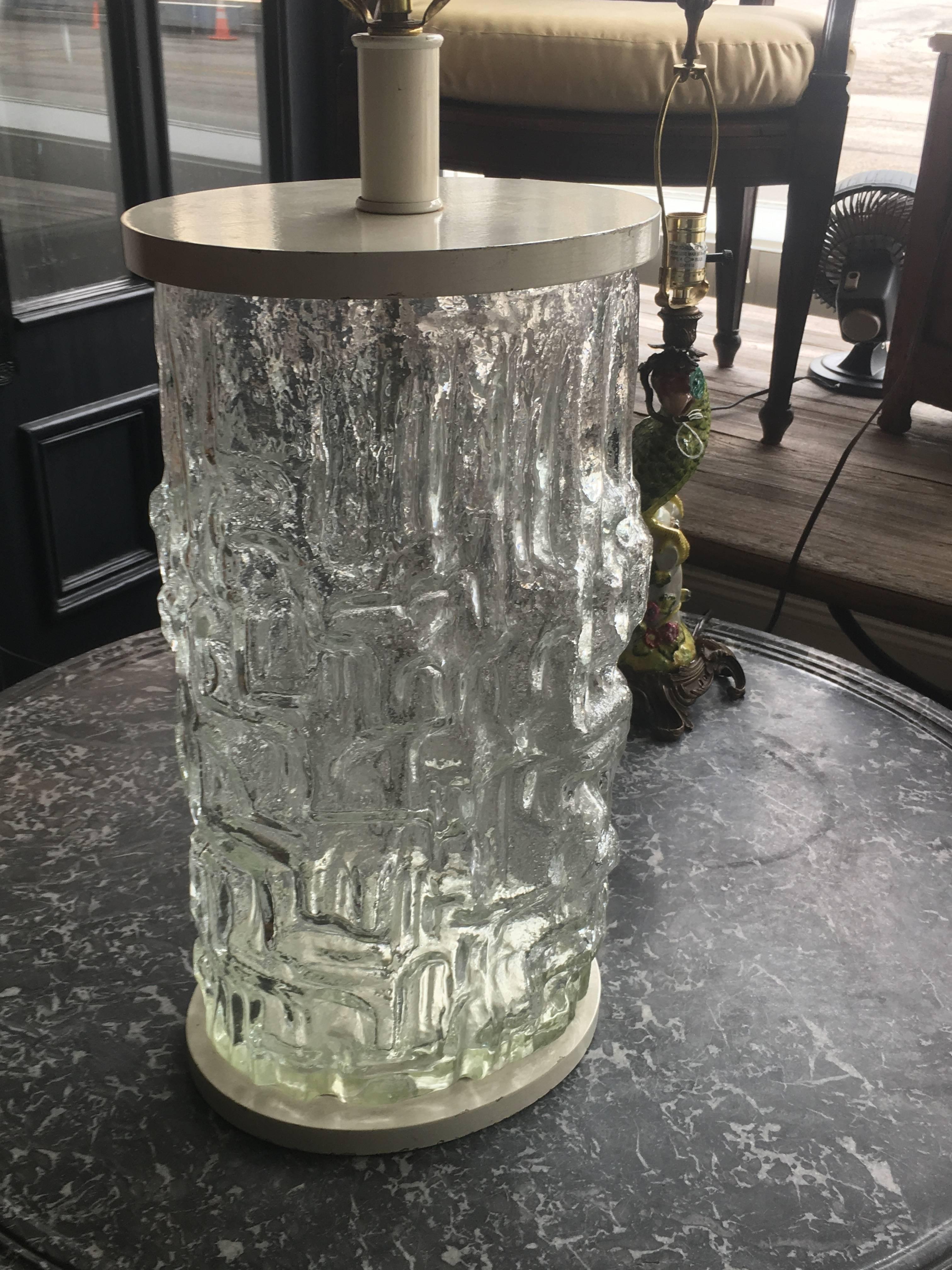 A Swedish glass vase
Midcentury
of cylindrical form with textured exterior, mounted as a lamp with cloth shade.
Measures: Height overall 38 1/4 inches.