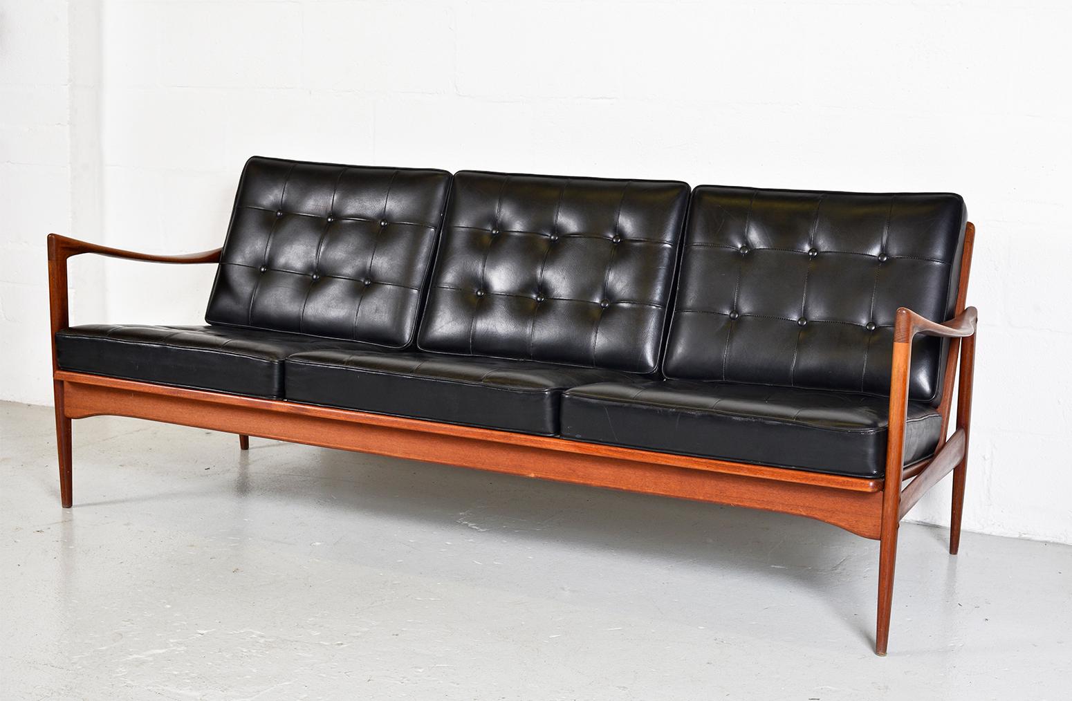 This highly sought after three-seat ‘Kandidaten’ sofa was designed by Ib Kofod-Larsen for OPE Möbler in the 1960s. Crafted to the very highest standards, its solid teak frame, open-sided, slat-back shape and sweeping armrests combined, will bring a