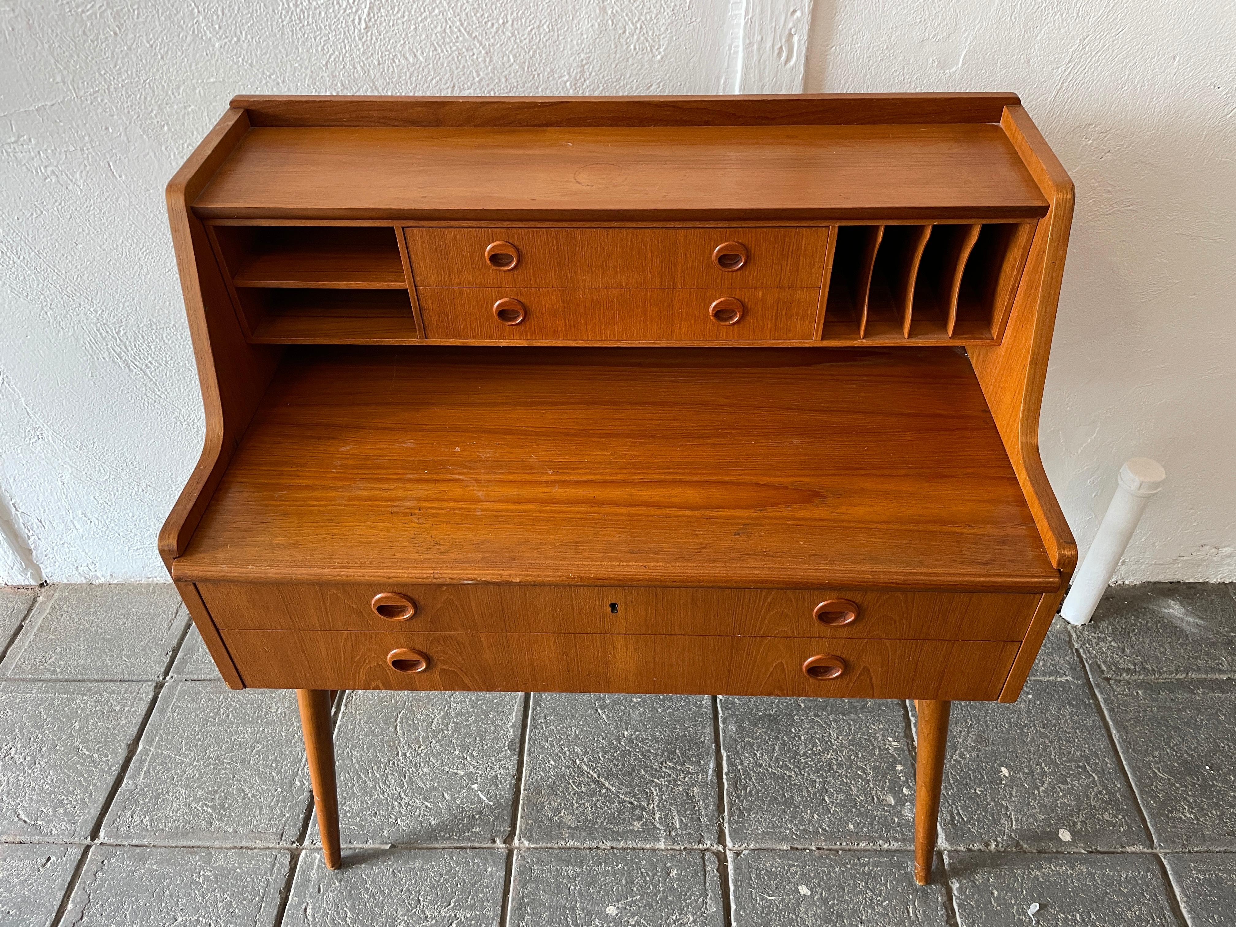 Swedish Mid-Century Modern teak desk with 4 drawers that have teak handles. Sits on tapered leg base. The drawers easily slide and are clean. original vintage condition and ready for use. Shows signs of use and patina. Desk surface slides forward