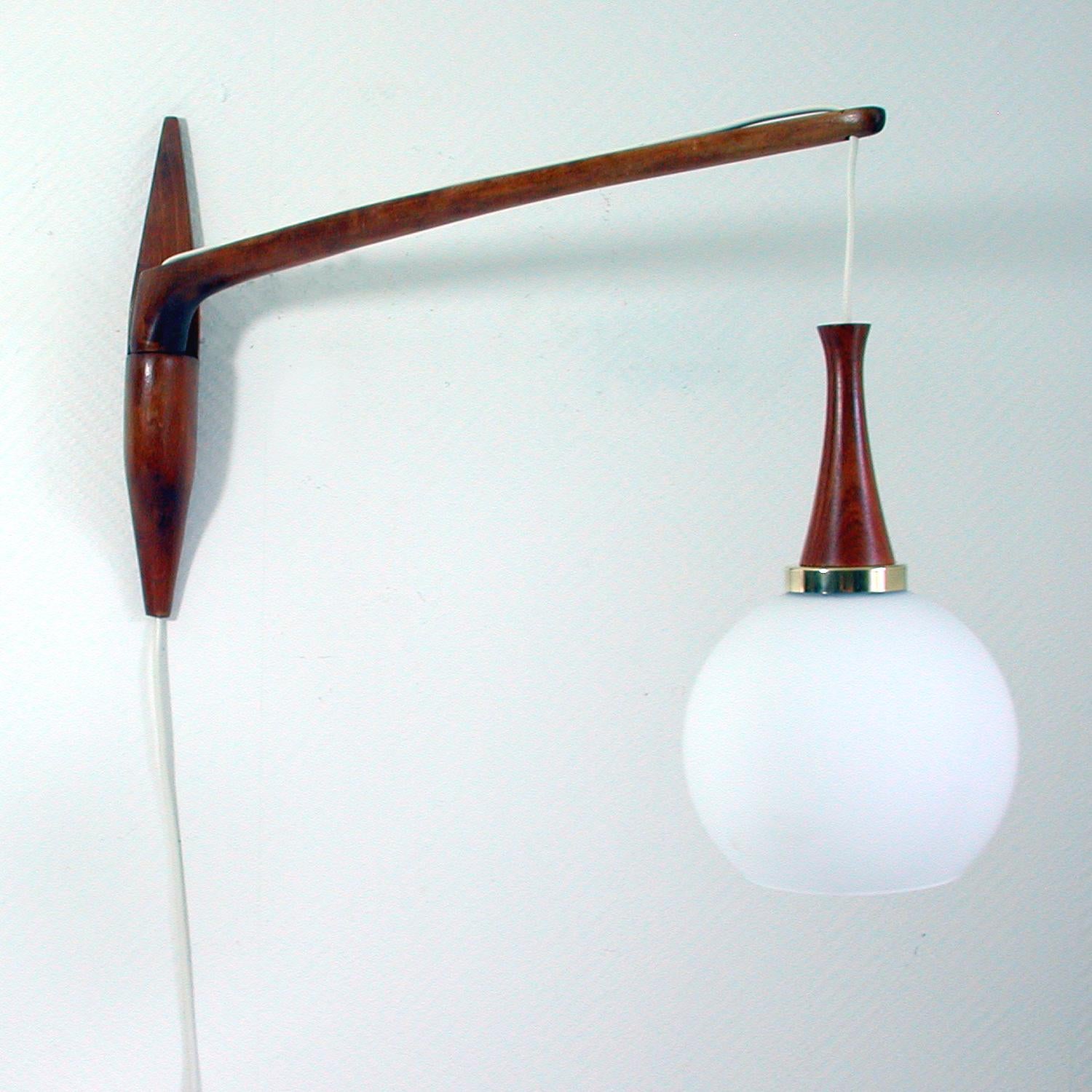 This elegant large midcentury wall light was designed and manufactured in Sweden in the 1960s in the Manner of Uno & Osten Kristiansson for Luxus. It has got a teak arm that swings left and right with a hanging milk glass shade. Diameter of