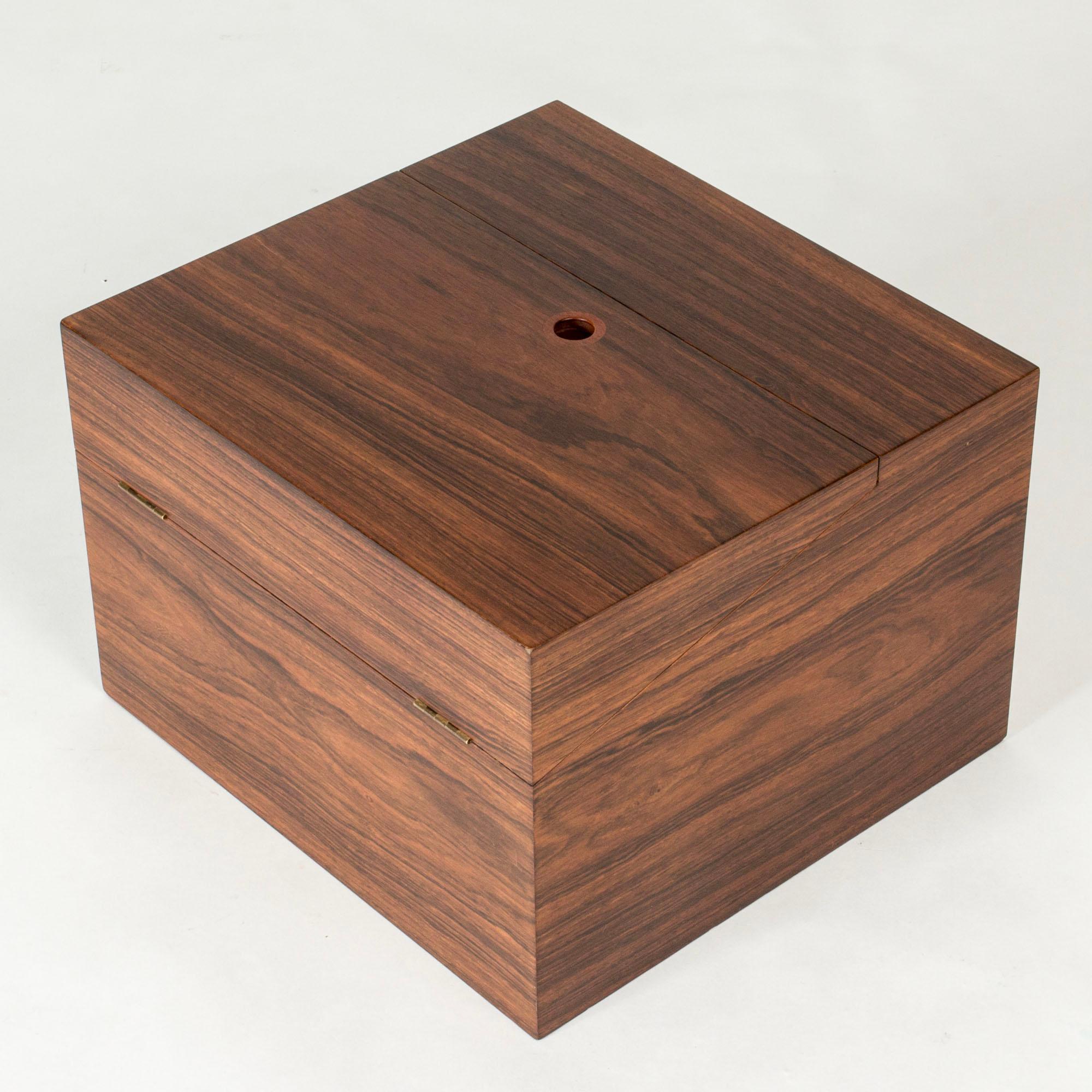 Mueble bar de Leif Alring con forma cuadrada, que se abre por la parte superior con un tirador redondo insertado. Chapa de palisandro, interior revestido de fieltro rojo.