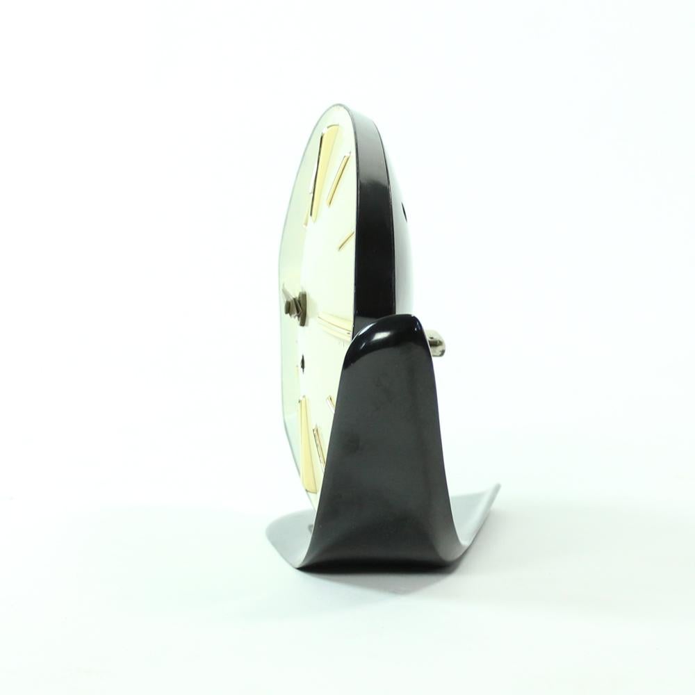 Rare midcentury table clock produced by PRIM clocks in 1950s. Great and very stylish item. Made of black bakelite construction and shell. The clock head is adjustable, standing on a brass ball. Original brass details. Cream/white clock face with