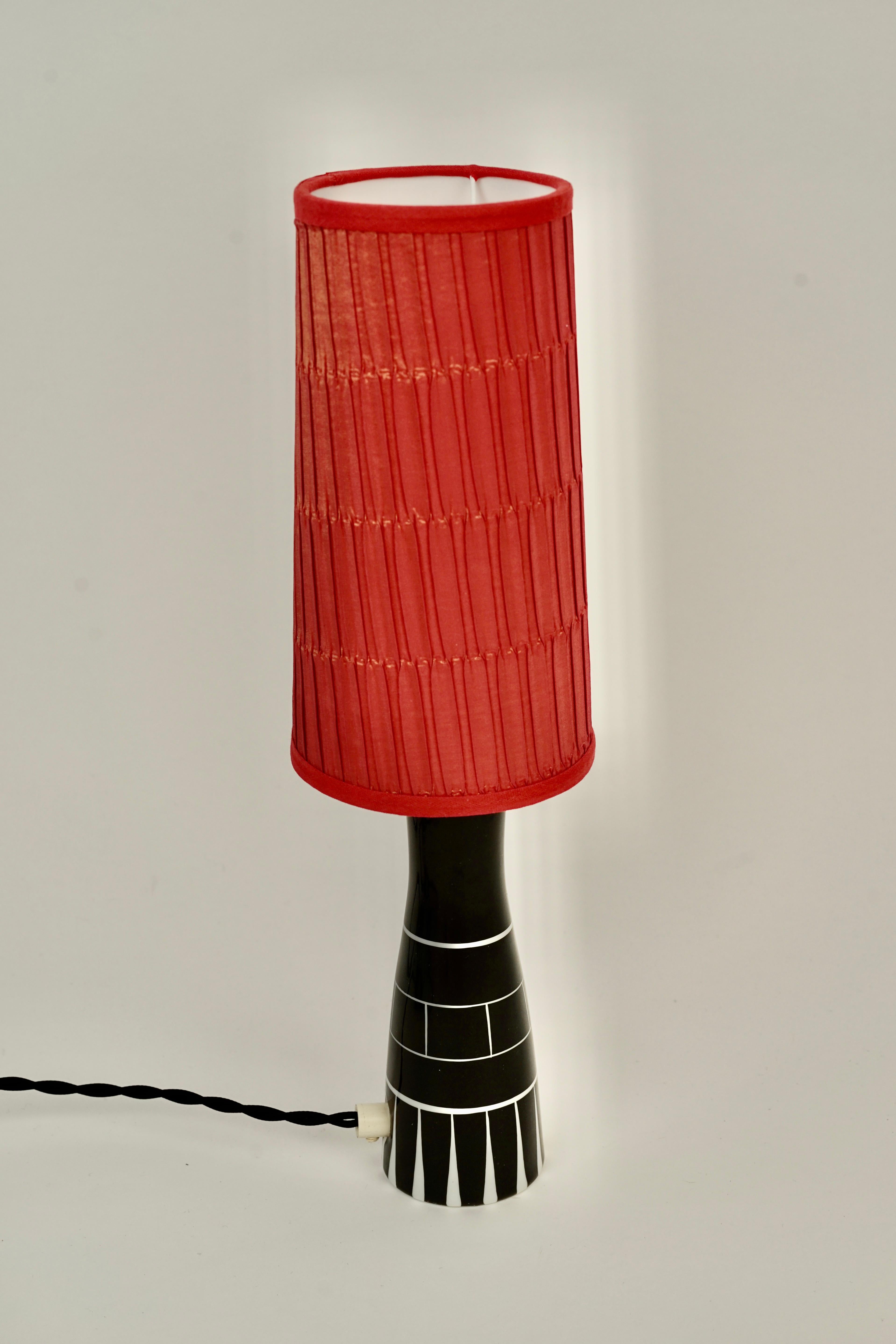 A rare midcentury table lamp from Royal Dux glazed in black with white pattern.
The lamp shade has been recovered in red silk using the original frame.
The silk has a beautiful iridescent  quality that exhibits itself in day light.

The shade is :