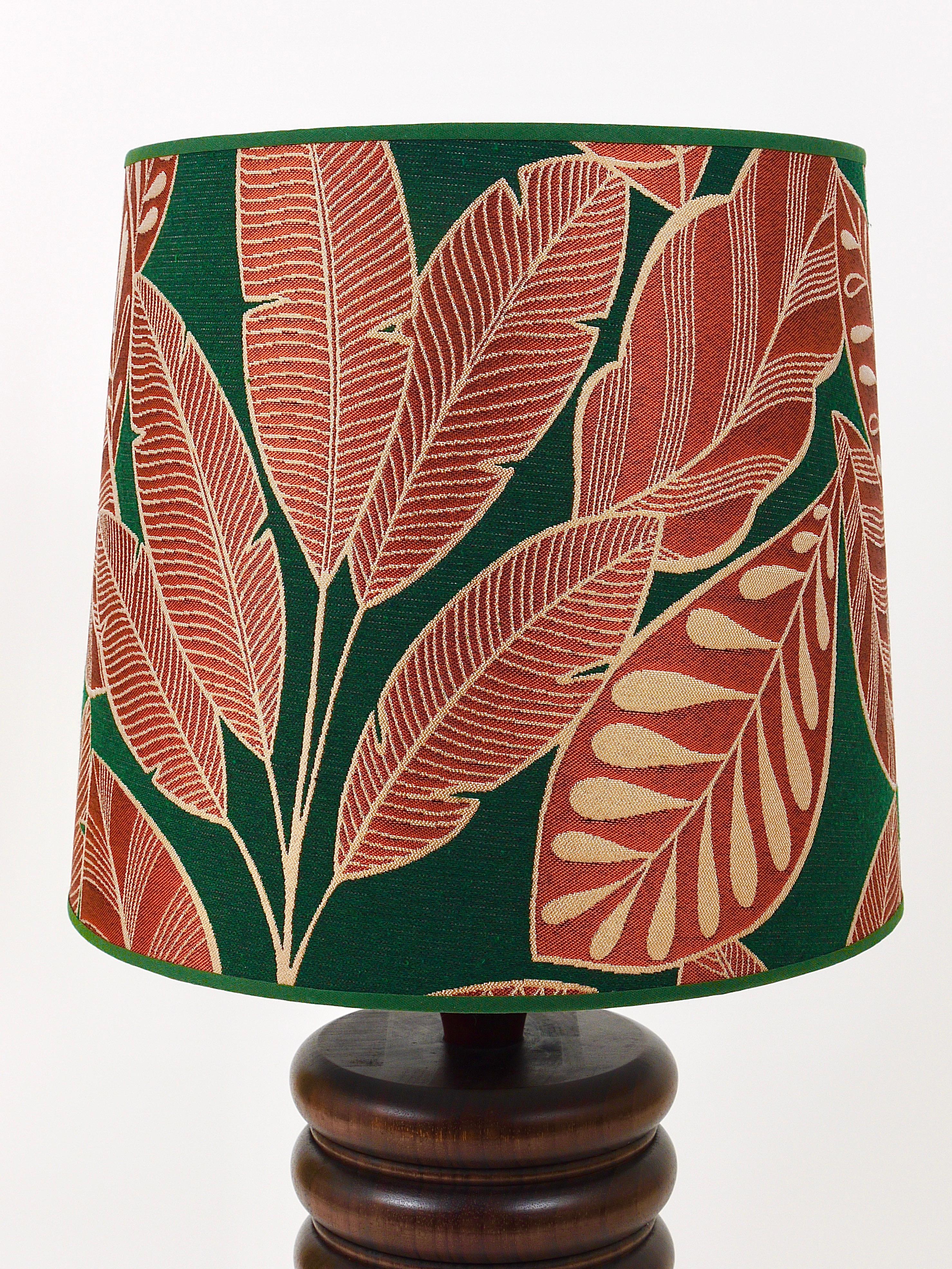 A beautiful table or side lamp from the 1970s with a turned base made of dark wood and a refurbished lampshade with a lovely premium leaf pattern fabric. A very decorative light in the style of Uno & Östen Kristiansson / Luxus. In very good