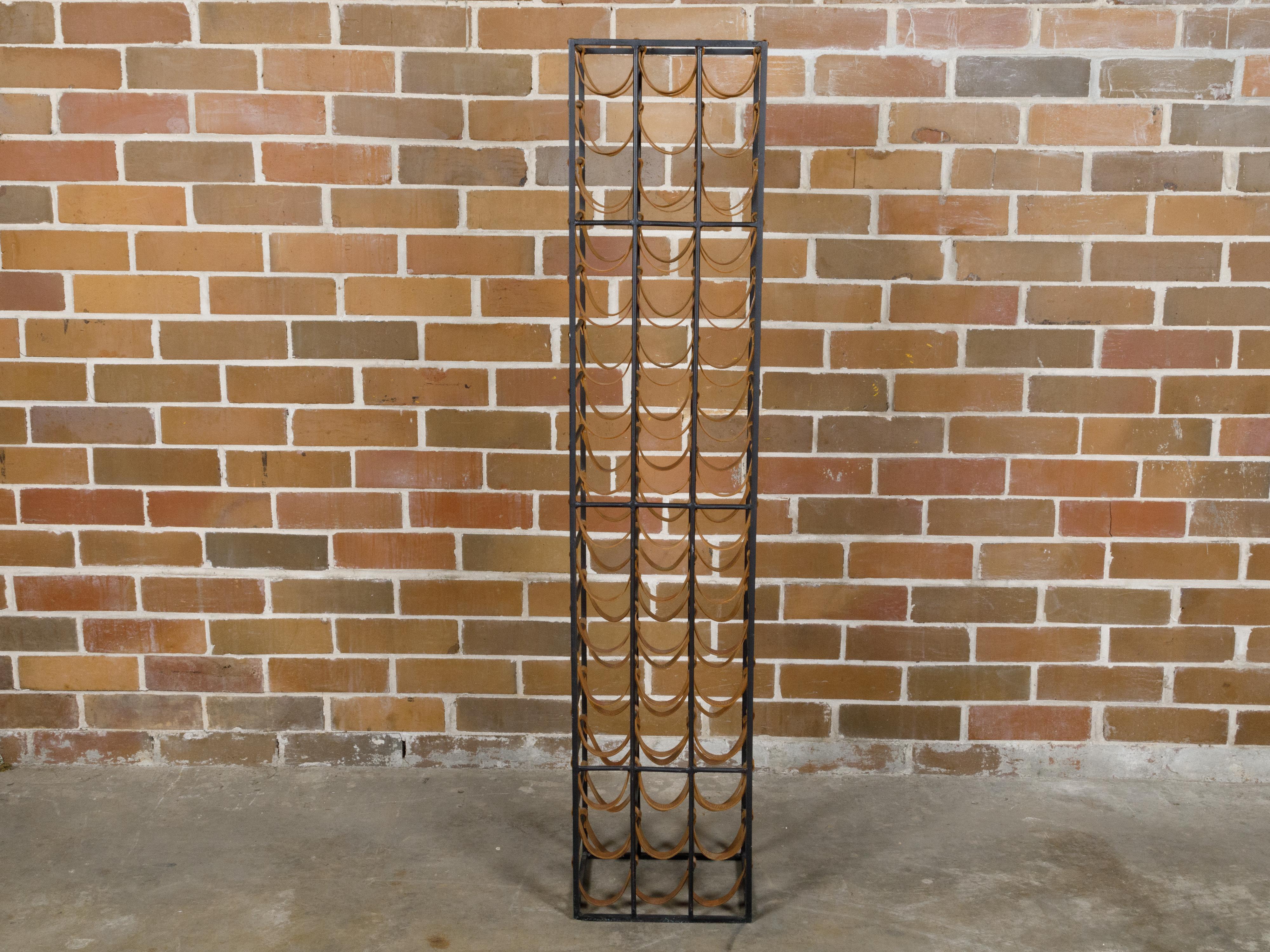 A tall and narrow Midcentury iron wine rack with leather straps. This Midcentury iron wine rack, distinguished by its tall and narrow silhouette, marries functionality with a touch of rustic elegance. Crafted from sturdy iron, it features a series