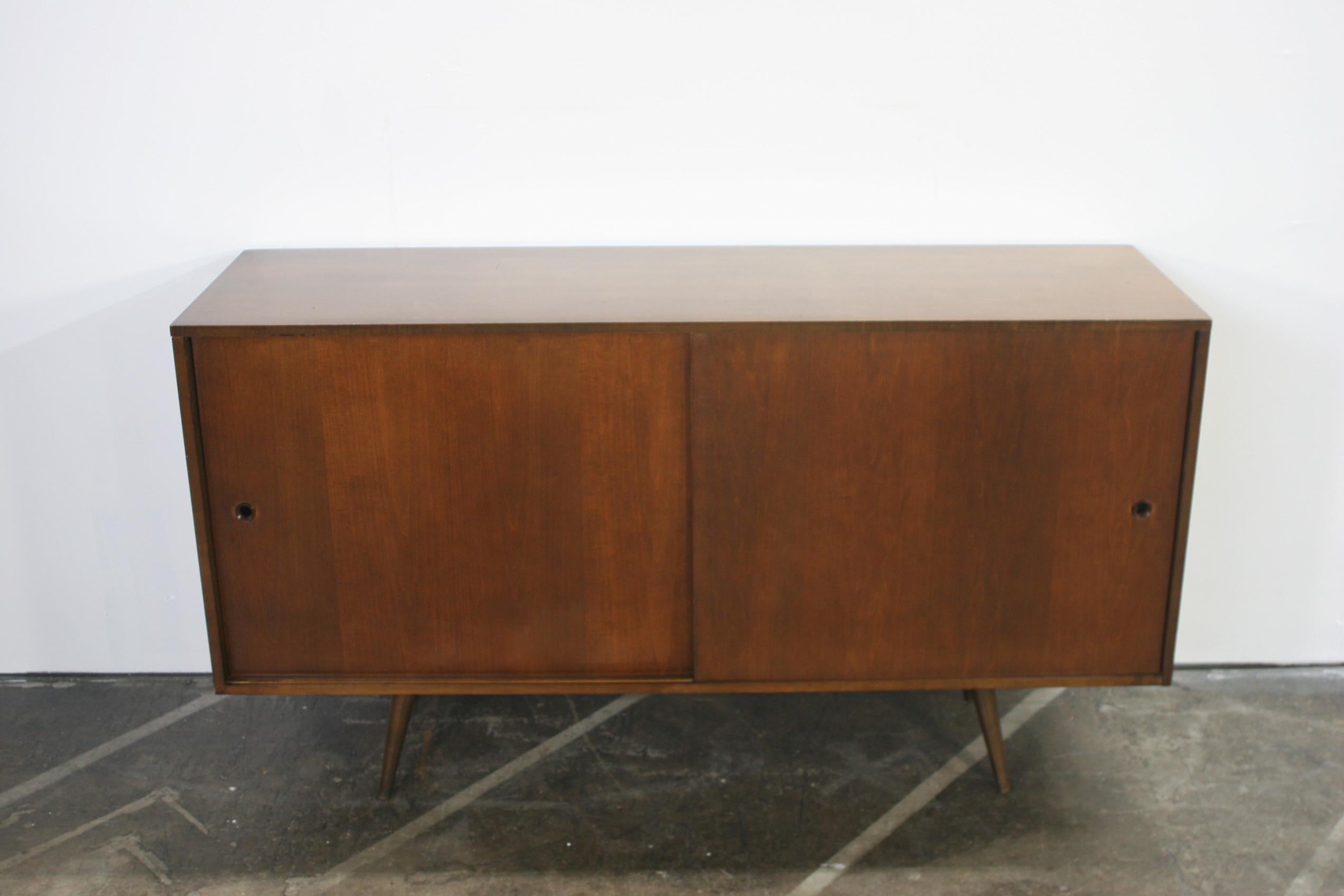 Beautiful mid-century tall credenza by Paul McCobb circa 1950 Planner Group #1514 has 1 adjustable shelves w/pins with 1 drawer on the left side and 3 drawers on the right side. Solid maple construction has a dark walnut finish. All original walnut