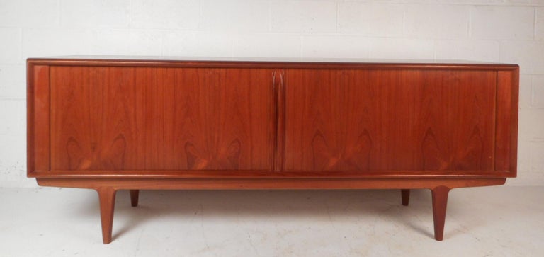 This stunning Mid-Century Modern sideboard features four drawers and two large compartments hidden behind tambour doors. Wonderful detail with a rich teak finish, sculpted door pulls, and tapered legs. A well made Danish modern credenza by Svend