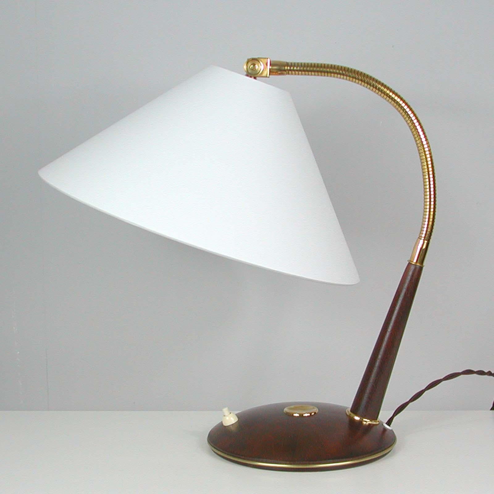 This large and elegant table lamp was designed and manufactured in Switzerland in the 1950s by Temde. It features a teak base with brass details, a brass gooseneck lamp arm and a new handmade off white silk lampshade. 

The light requires one E27