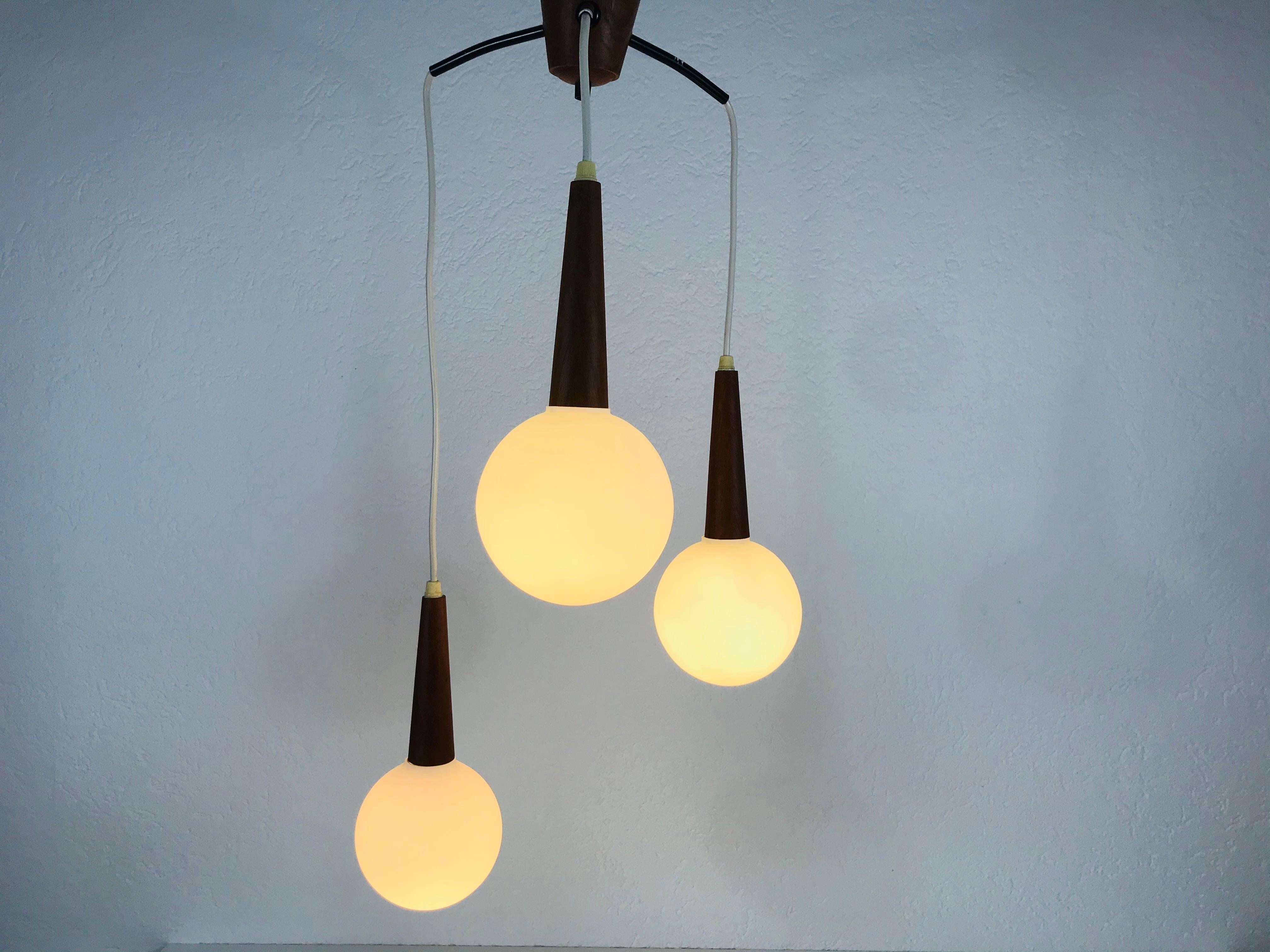 A teak and white opaline glass ceiling light made in the 1960s in Sweden. Three glass shades secure to the teak body. The glass shade is made of thin opaline glass and ball shape. The lamp has a Scandinavian design and is attributed to the Swedish