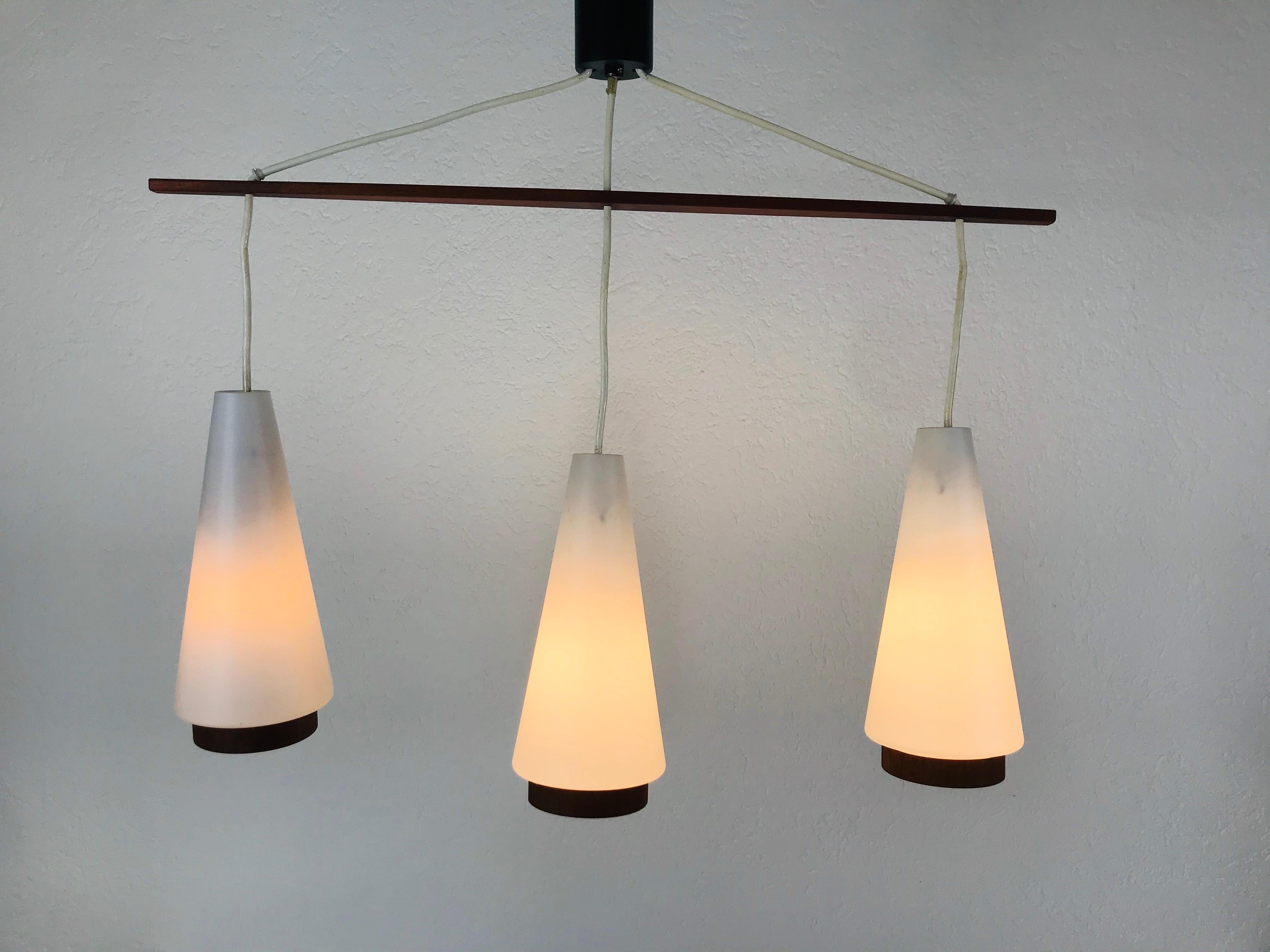 A teak and white opaline glass ceiling light made in the 1960s. Three glass shades secure to the teak body. The glass shade is made of thin opaline glass and has cylinder shape. The lamp has a Scandinavian design.

The light requires three E27