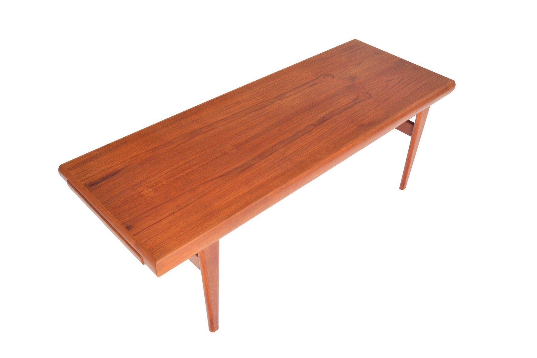 This Danish modern teak coffee table appears simple but is designed with ingenious functionality. The large teak top offers a round form and holds a teak tray on one side. The opposing end features a collapsible side table crafted with the same
