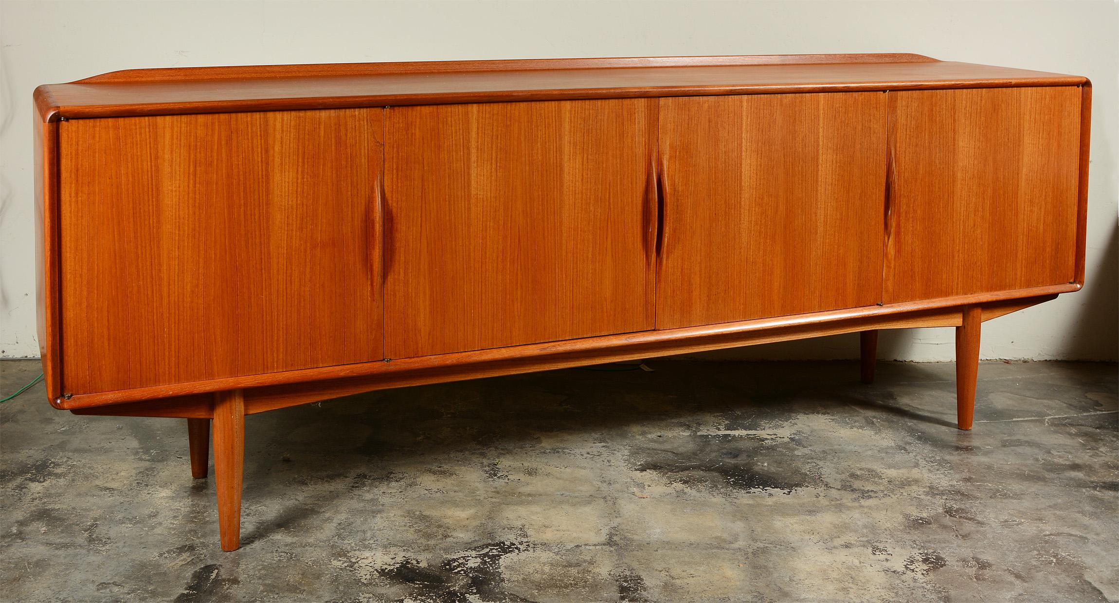 Sleek Norwegian teak credenza by Alf Aaseth for Gustaf Bahus. This has sculptural handles, rounded corners and a raised lip across the back of the top. There are four doors concealing one long shelf in the center and three small drawers and one