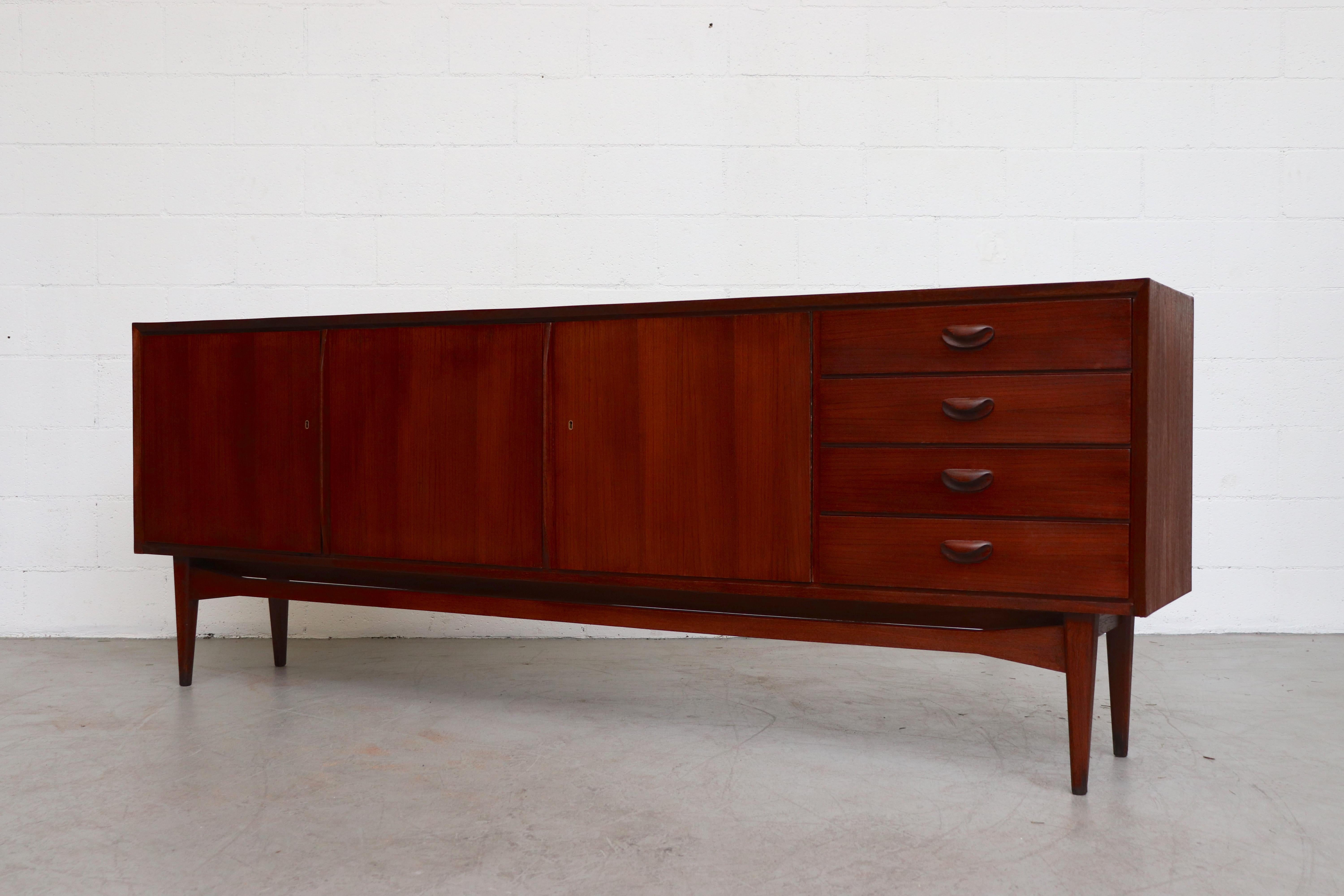 Midcentury teak credenza. Handsome warm toned teak with three large cubbies and four drawers with organically carved drawer pulls. In good original condition with some visible signs of wear consistent with age and use.