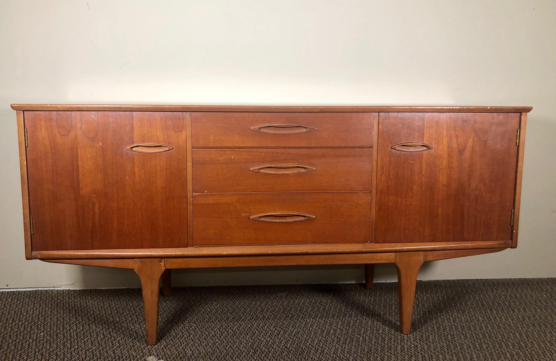 1960s credenza by Jentique. Made in England.

Three drawers in the middle flanked by a cabinet with a fixed shelf on either side.

Very good condition. Minor marks on the top. Small chips and scuffs here and there from normal use. Please see