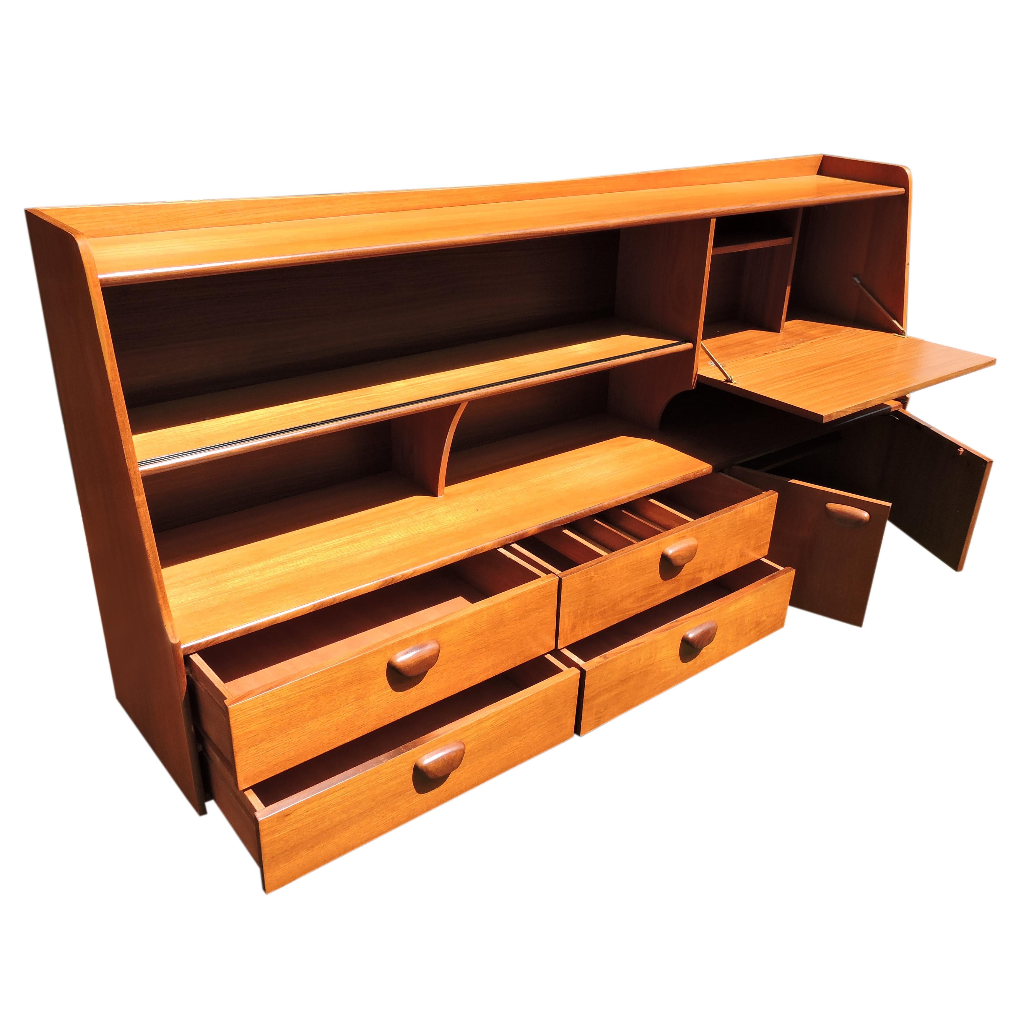 - Teak high board by British manufacturers Portwood
- Comprised of sliding glass doors above an open shelf
- Features a pull-down lockable leaf with shelving 
- Has two opening doors below with and three drawers
- Finished with teak pull handles.