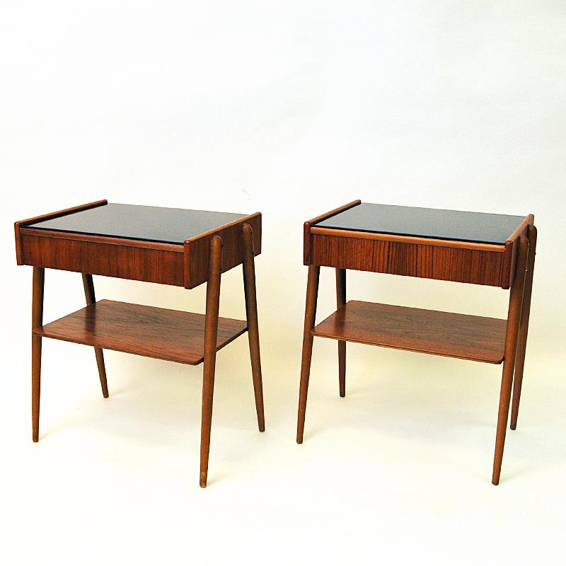 Great pair of teak and glasstop bedside /sidetables by AB Carlström & Co Möbelfabrik 1950s Sweden. The tables have a drawer and sligthly tilted A- shaped legs. The table tops with black painted shiny glassplates on the surface and a teak shelf