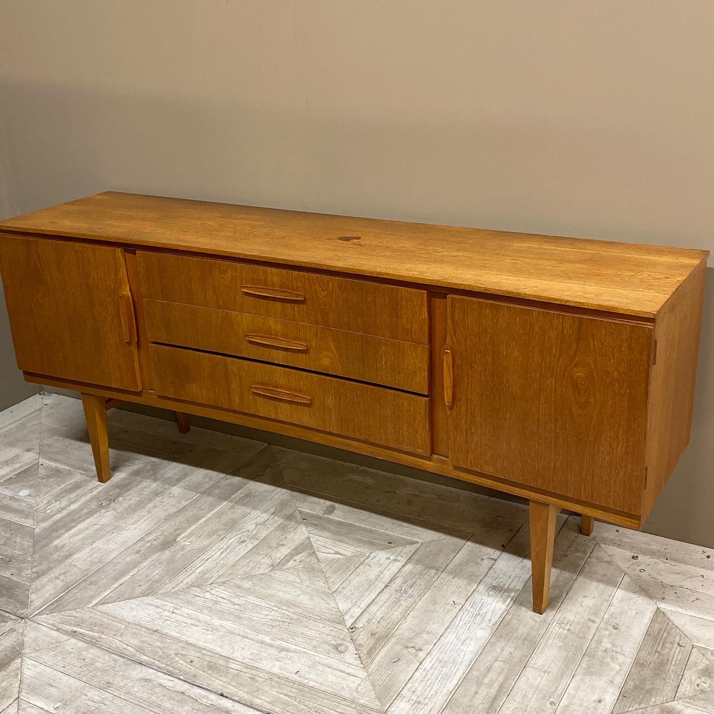A concave midcentury teak sideboard by Beautility. The concave shaped top with three central drawers below, flanked by two cupboards with enclosed shelves. The whole standing on square tapered legs. Attractive handles adorn the drawers and doors.