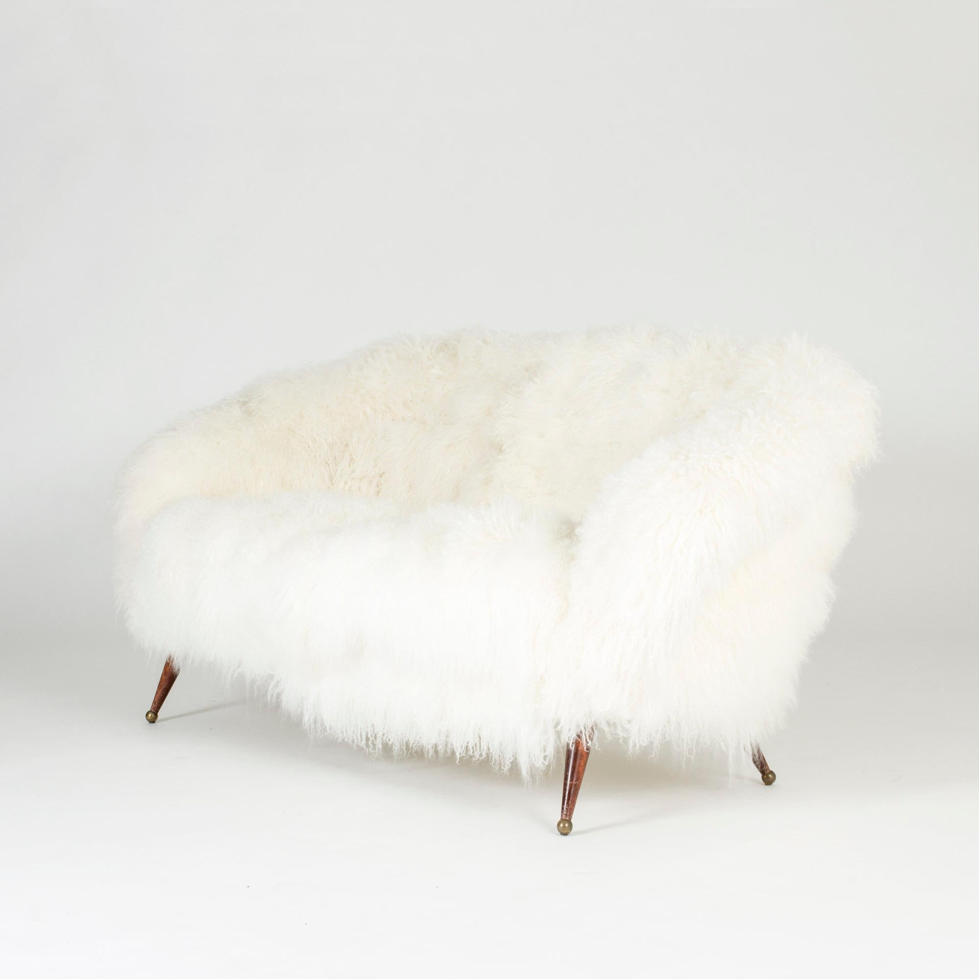Stunning “Tellus” sofa by Folke Jansson, upholstered with white, long, wavy sheepskin. Rounded, wide and low design with slender legs with brass balls as feet.