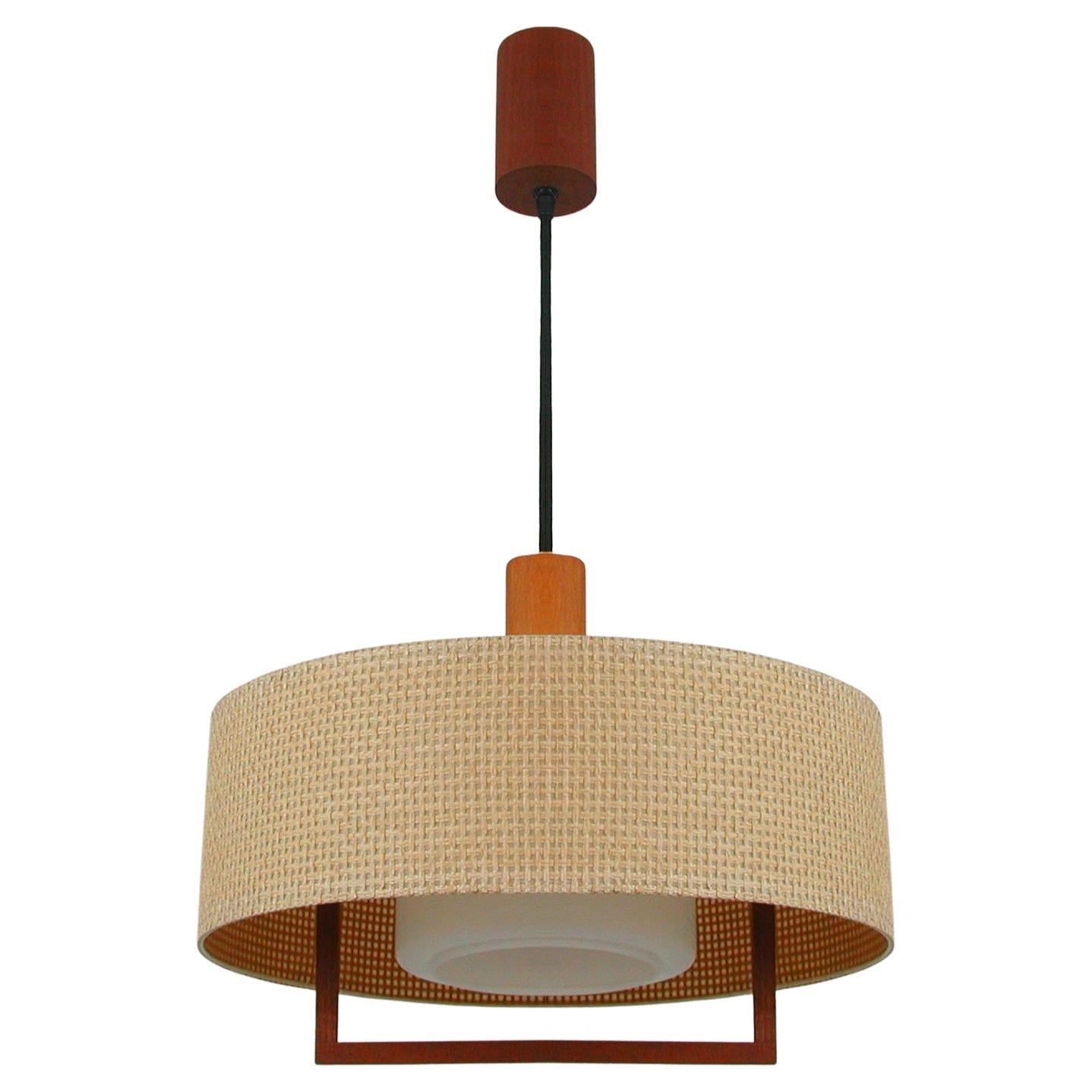 This unusual Mid-Century Modern pendant was designed and manufactured by TEMDE Leuchten in Switzerland in the 1960s.

It features a large round raffia lamp shade, a white milk glass diffuser and teak details. 

The light requires one E27 bulb up