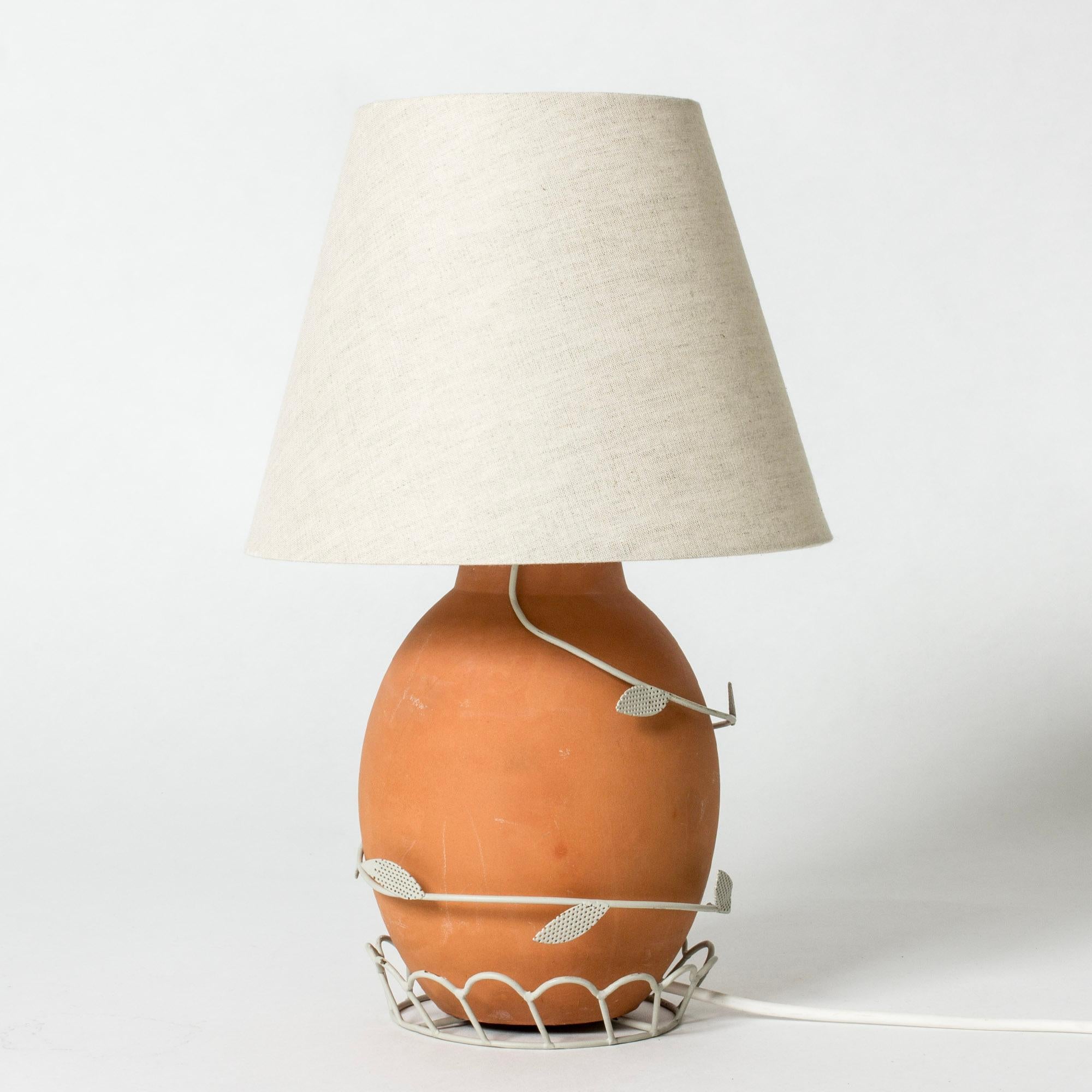 Lovely table lamp from Corona Belysningskultur, with a terracotta base. Decor of a white lacquered frame enveloping the base, with a scalloped pattern and leaves.