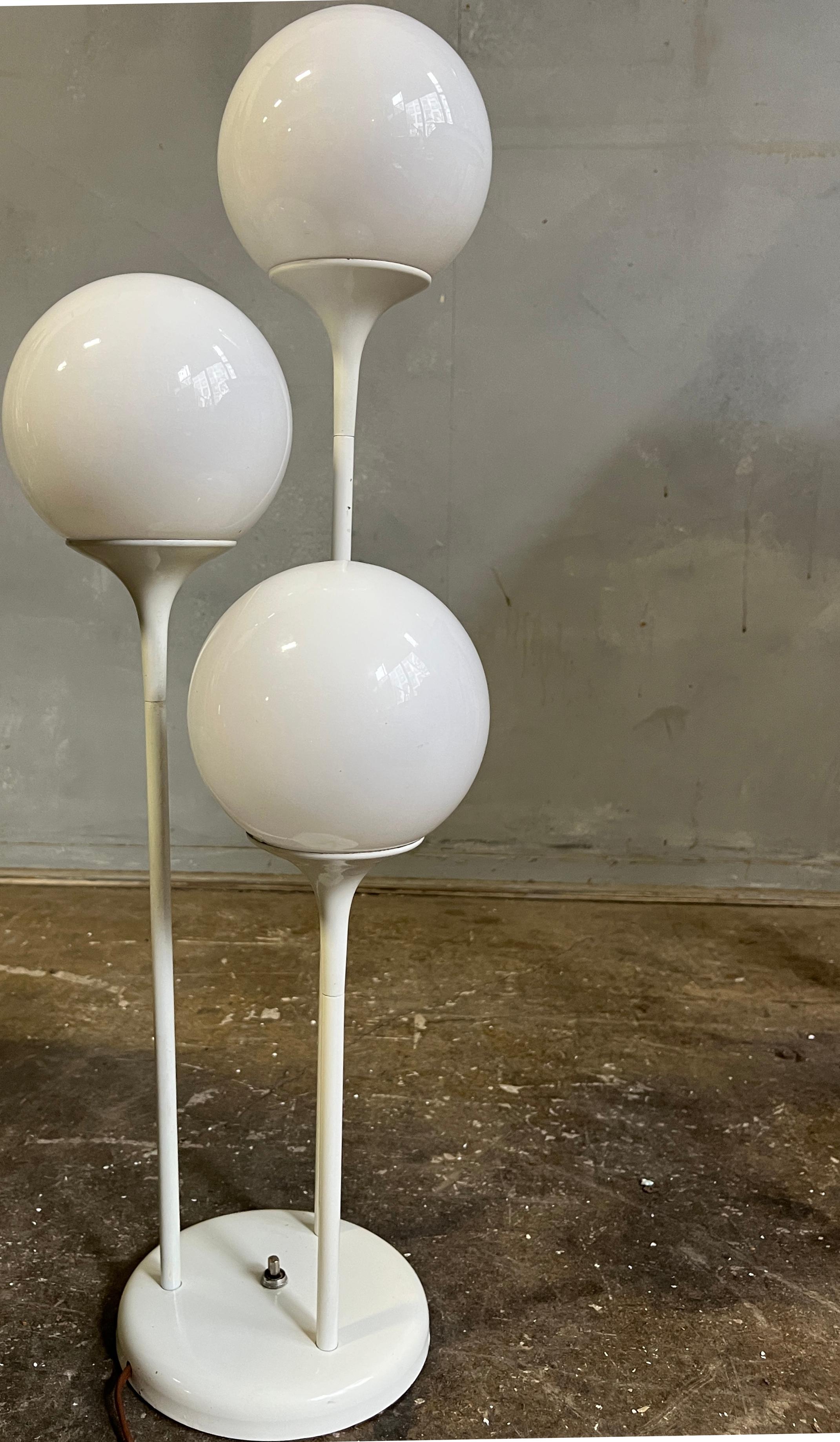 An uncommon white enameled floor lamp with three white glass globes on metal stems that mimic popular architectural themes of the period, namely Eero Saarinens' tulip style hourglass forms.   Lamp is heavy and sturdy due to being solid metal.