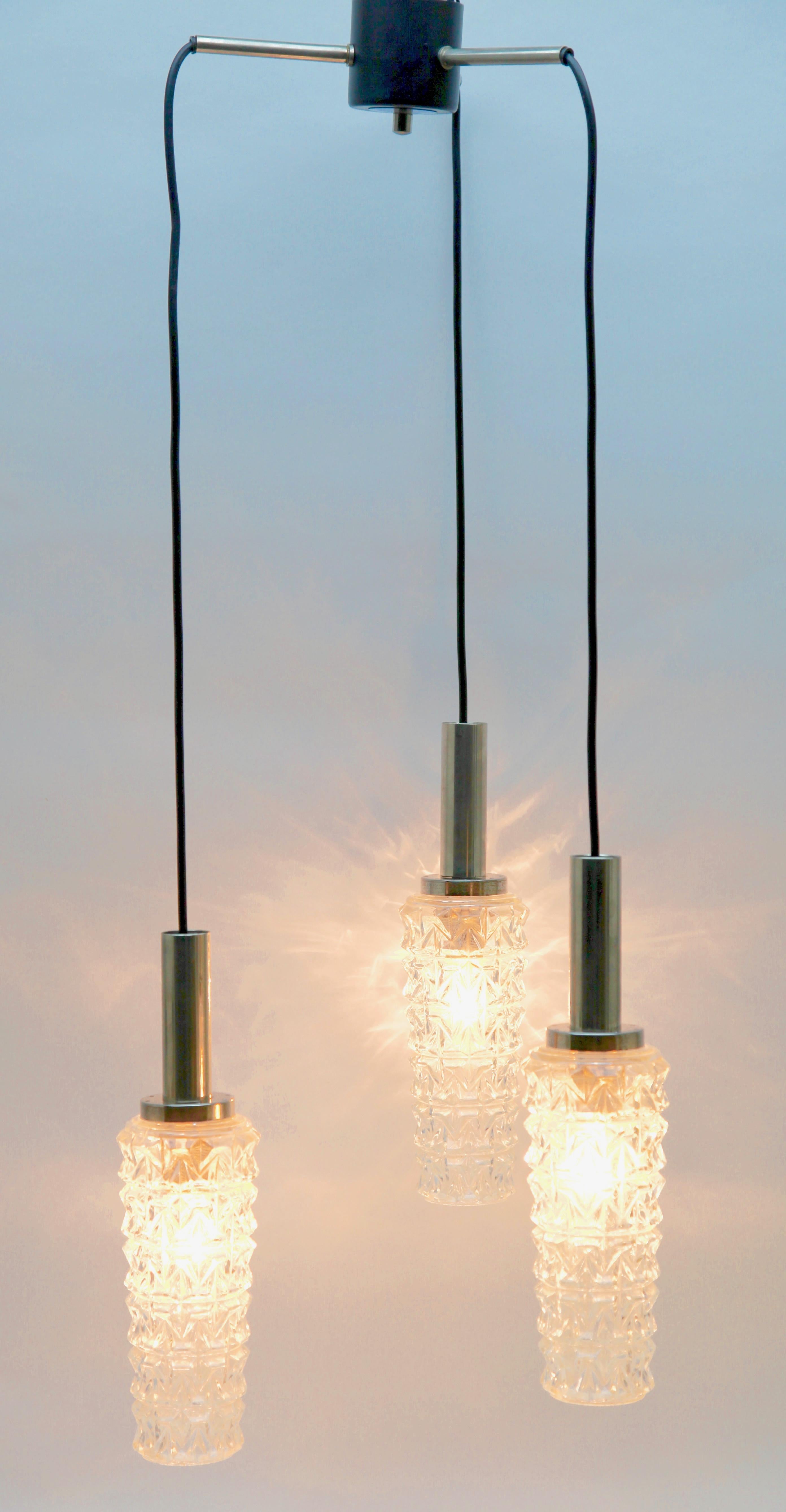 Lampe suspendue chromée du milieu du siècle à trois câbles avec flexibles réglables, ce qui permet de suspendre les lampes à différentes hauteurs en rétractant les câbles dans la plaque de plafond. Les trois lampes sont maintenues par une simple