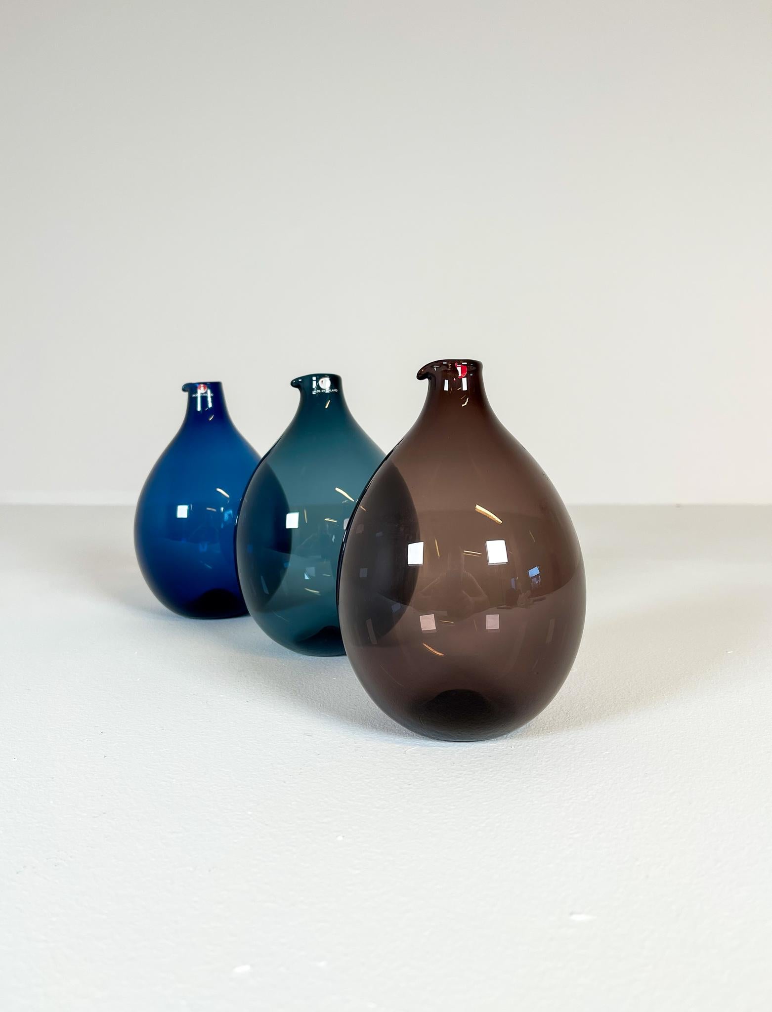Wonderful sculptured bottled handmade in colored glass. This set in three different colors. 
The bottles were produced by Iittala in 1956-1962 and designed by Timo Sarpaneva. 

Fully signed in the bottom of them. 

Measures H 16 cm, D 12 cm.