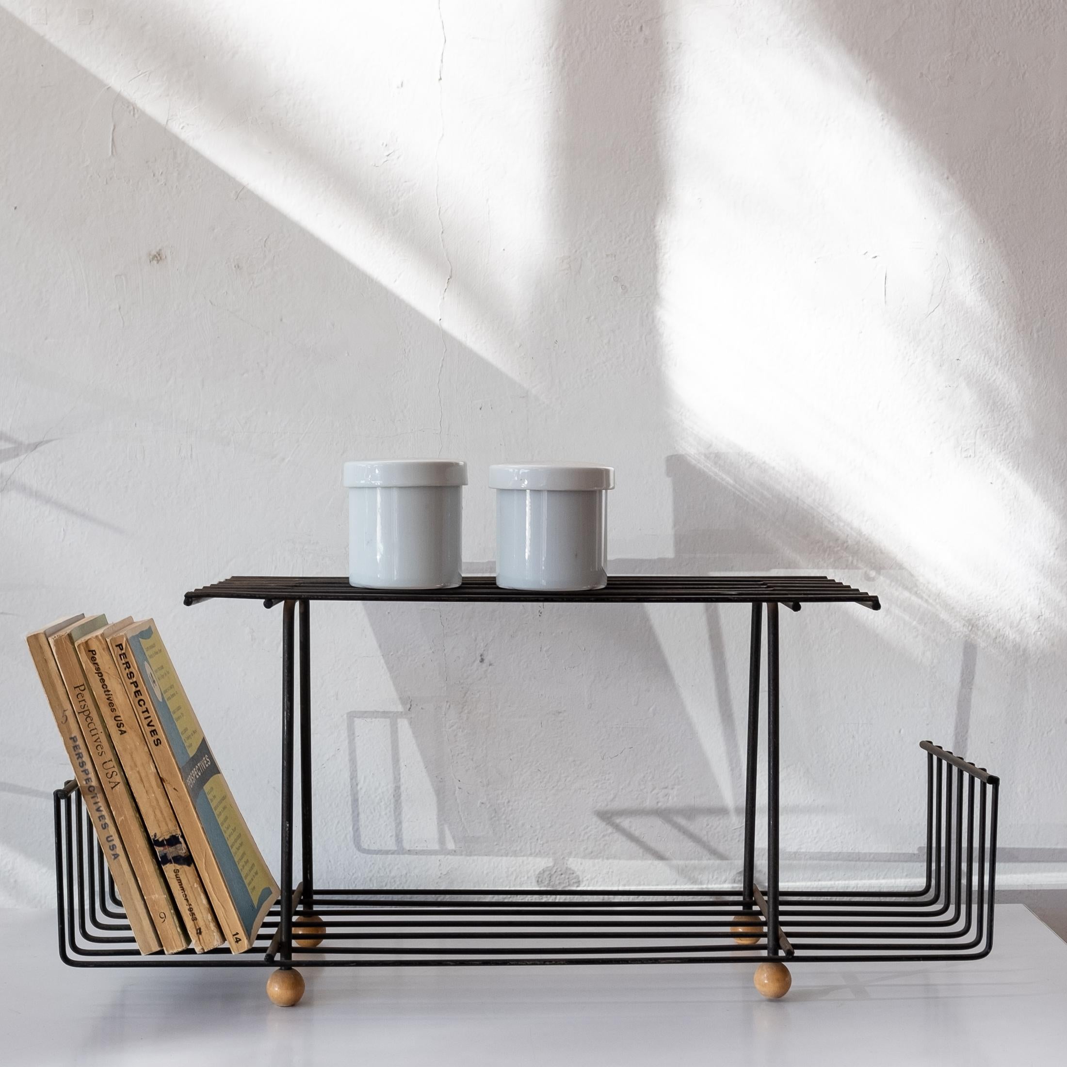 Tabletop or wall-mounted shelf by industrial designer Tony Paul. Iron structure will solid wood ball feet. Great for on a cabinet or mounted on a wall. 

Tony Paul studied at Brooklyn Polytechnic and majored in design at Pratt Institute. Before