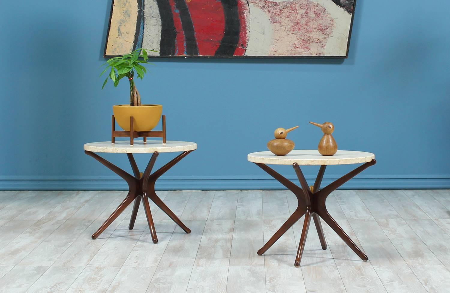 A pair of side tables designed and manufactured in Italy circa 1950’s. The beautiful cream-colored travertine tops show minor wear from age and contrast exquisitely with the dark walnut wood jax-shaped bases that are adorned with a brass pin in the