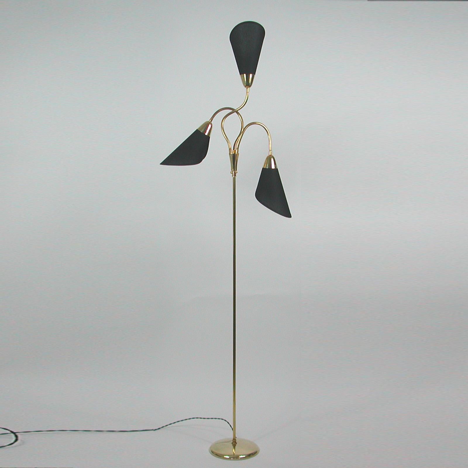 This unusual mid-century brass gooseneck floor lamp was made in Germany in the 1950s.

The lamp features a round brass base and three adjustable gooseneck lamp arms with handmade black cotton shades. The fabric shades have been refurbished and the