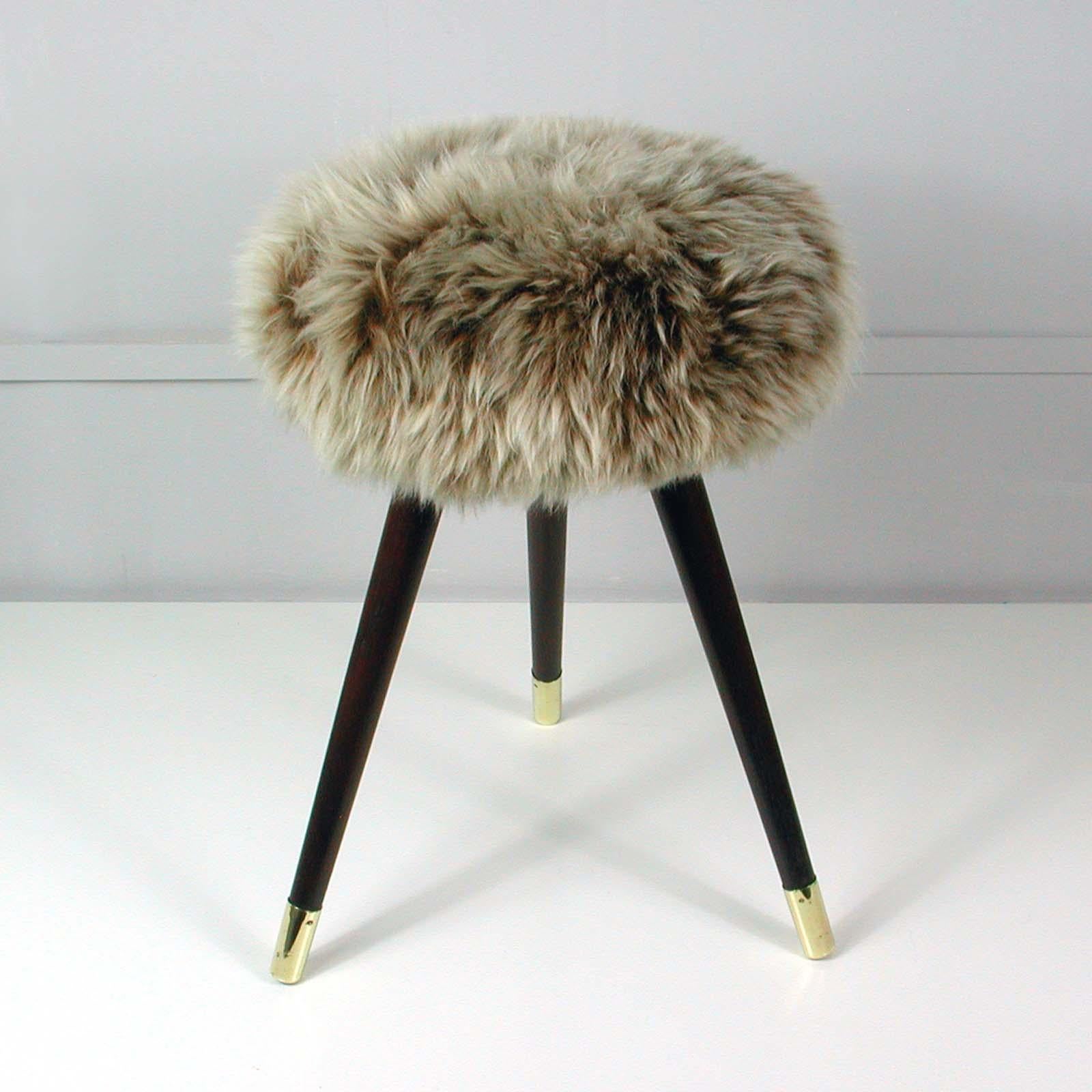 Midcentury tripod stool dating from the 1950s. Designed and manufactured in Germany.

The stool features three tapered walnut legs with brass tips and a dark brown and cream flamed real Iceland lamb fur seat. 

It has been completely restored,