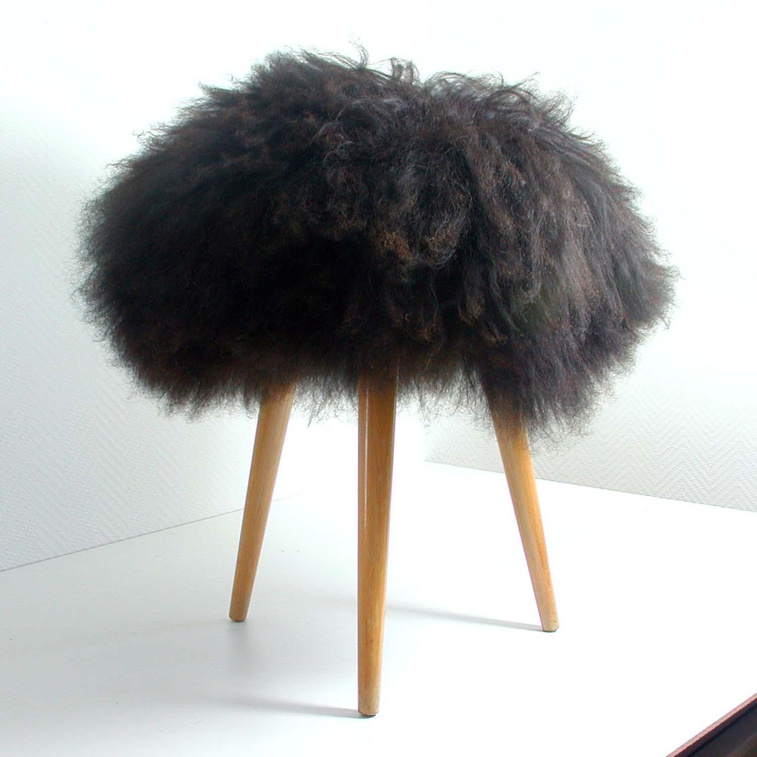 Midcentury tripod stool dating from the 1950s. The stool has got three tapered beechwood legs and a dark brown real Iceland lamb fur seat. 

It has been completely restored: the wooden legs re-lacquered and the seat upholstered. The fur is new.
