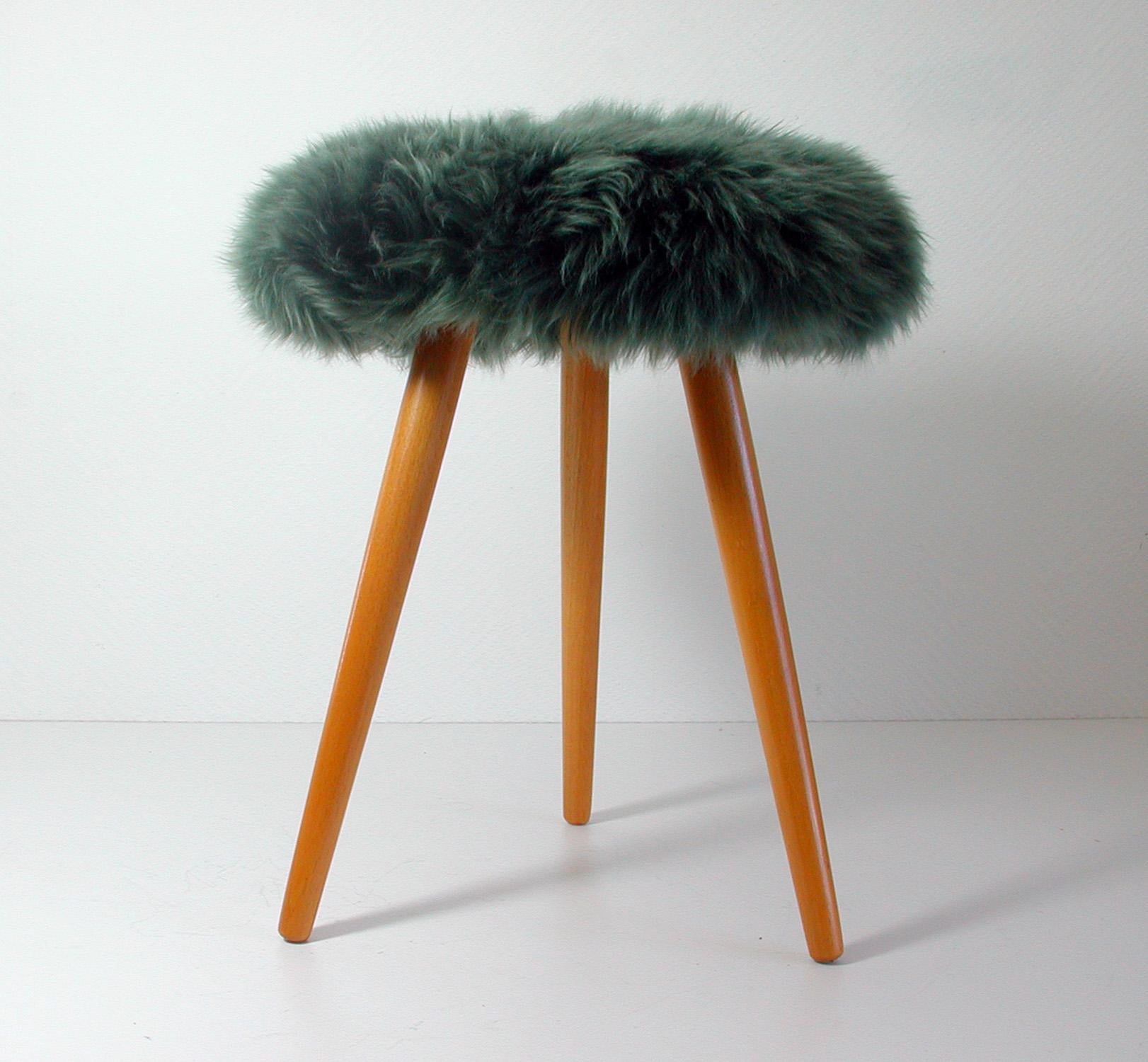 Midcentury tripod stool dating from the 1950s. The stool has got three tapered beechwood legs and a forest green real Iceland lamb fur seat. 

It has been completely restored: the wooden legs partly re-lacquered and the seat upholstered. The fur