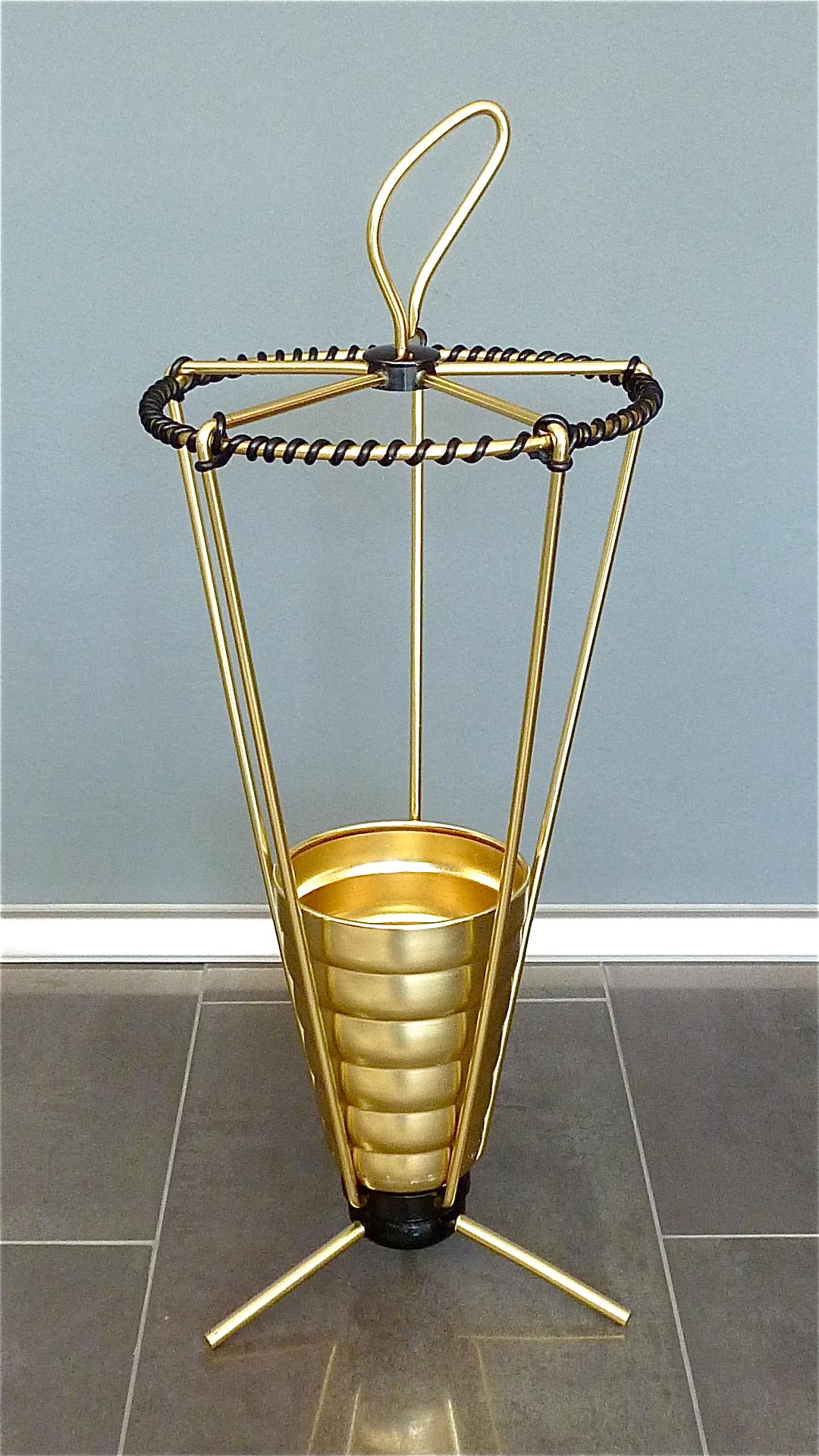 Midcentury golden anodized aluminum umbrella stand with black enameled iron weighted tripod sputnik base, a golden beaker as raindrop-catcher and black plastic cord wrapping around the rim, Italy, circa 1955. Very good original condition, minor