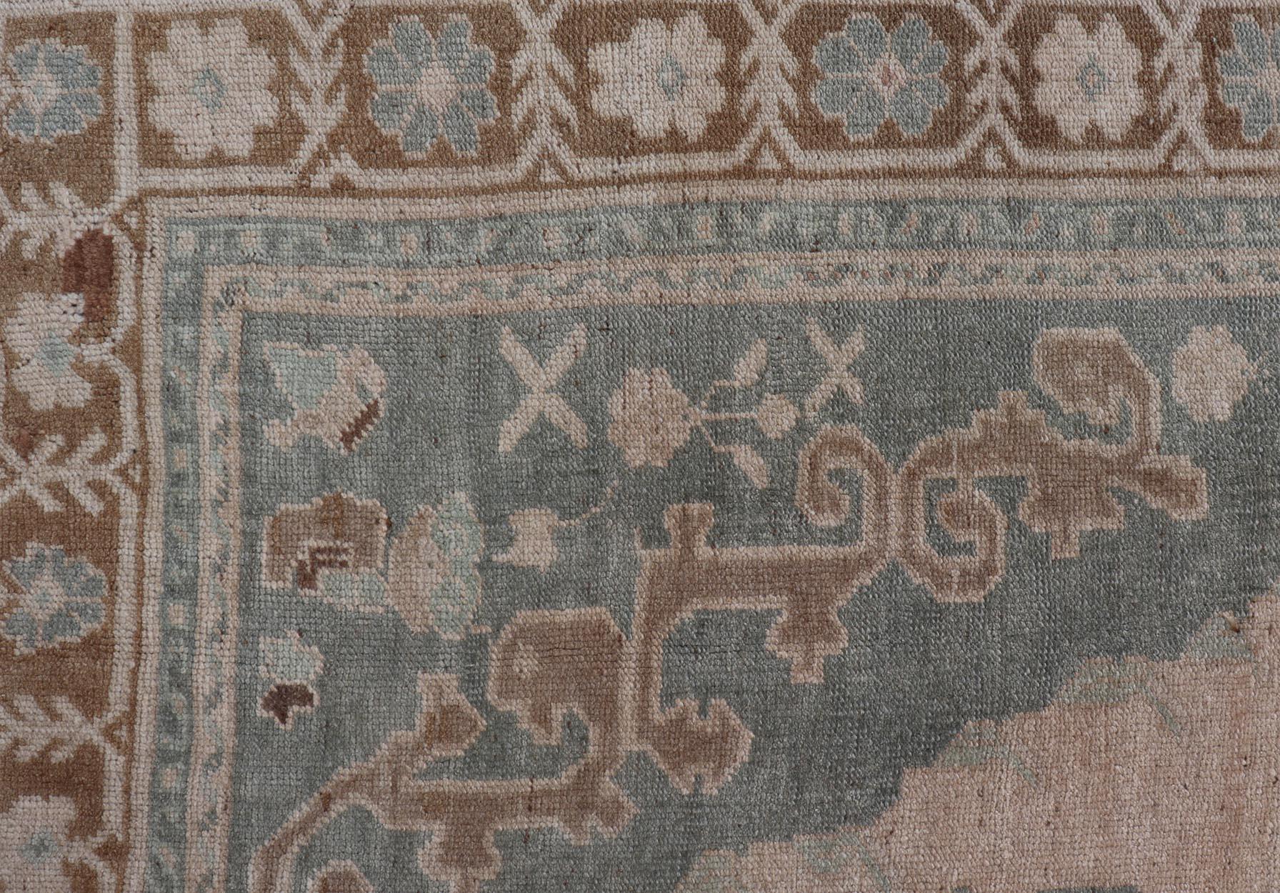 This Turkish Oushak rug has been hand-knotted in wool and features a sub-geometric etched medallion design rendered in cream, blue and taupe tones. A complementary, multi-tiered border encompasses the entirety of the piece; making it a marvelous fit