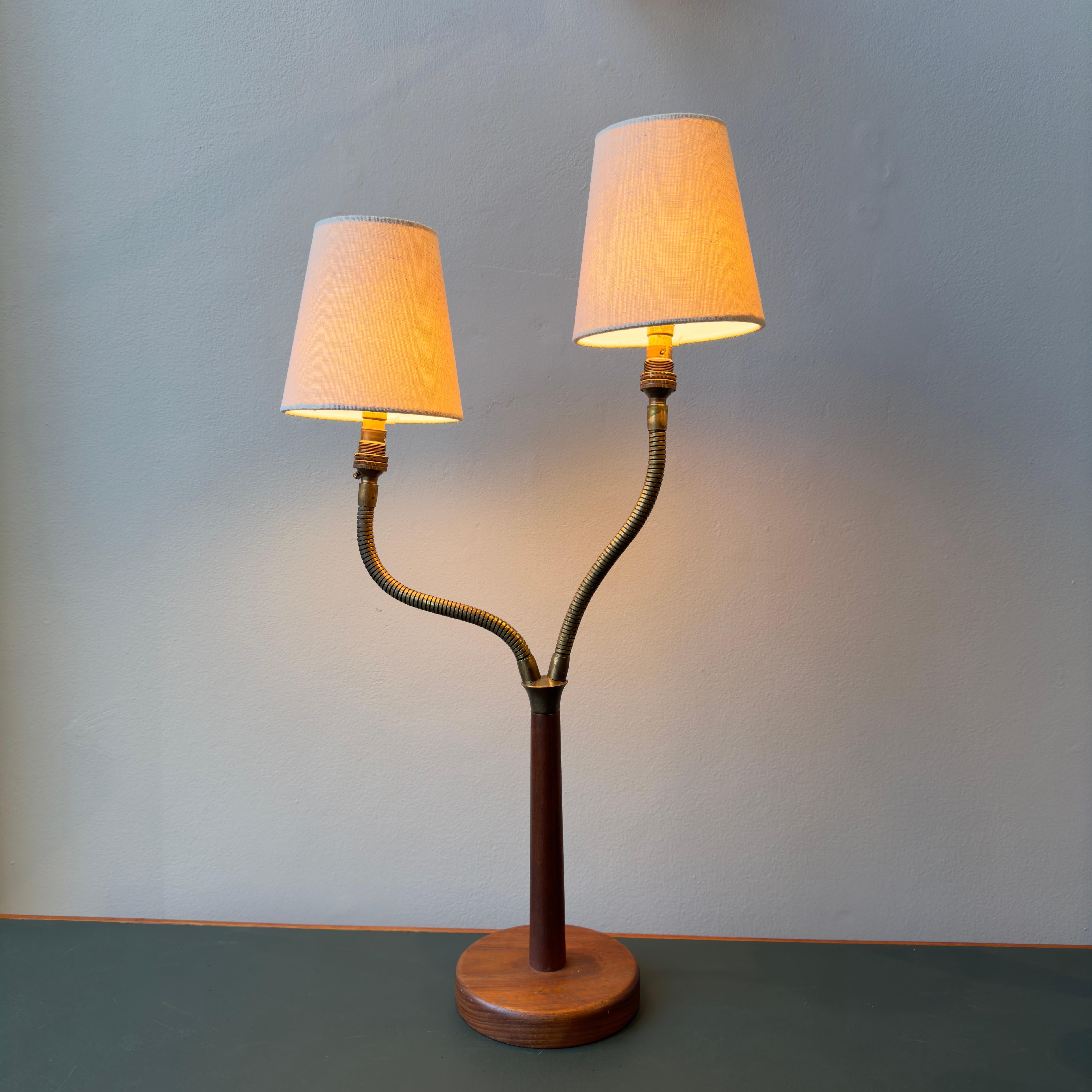 Made in Denmark during the 1950s, this twin headed table lamp is petite, yet sculptural. 

The base is fully teak, and supports two brass gooseneck stems which can be bent to your preference, whether that be simply symmetrical or playfully