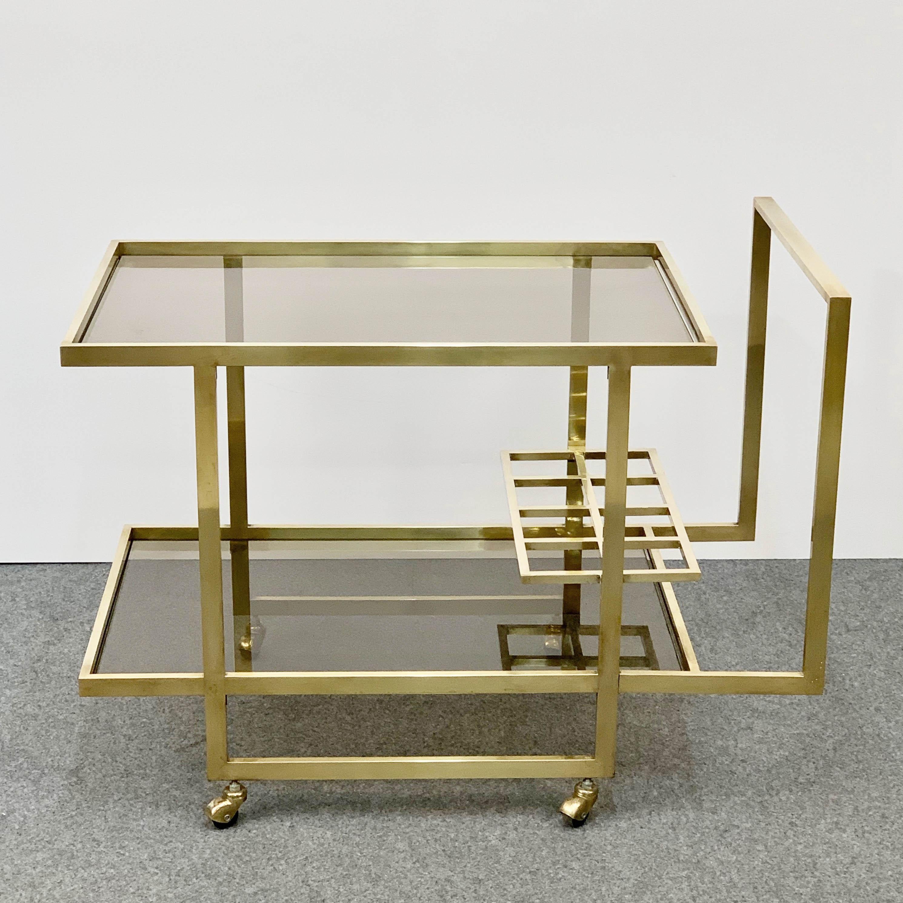 Exceptional two-level service midcentury brass cart produced in Italy during 1970, with bottle holder.

The brass is gold-plated and the glass is lightly smoked, with a perpendicular design the represents Italy during the 1970s at its best.

A