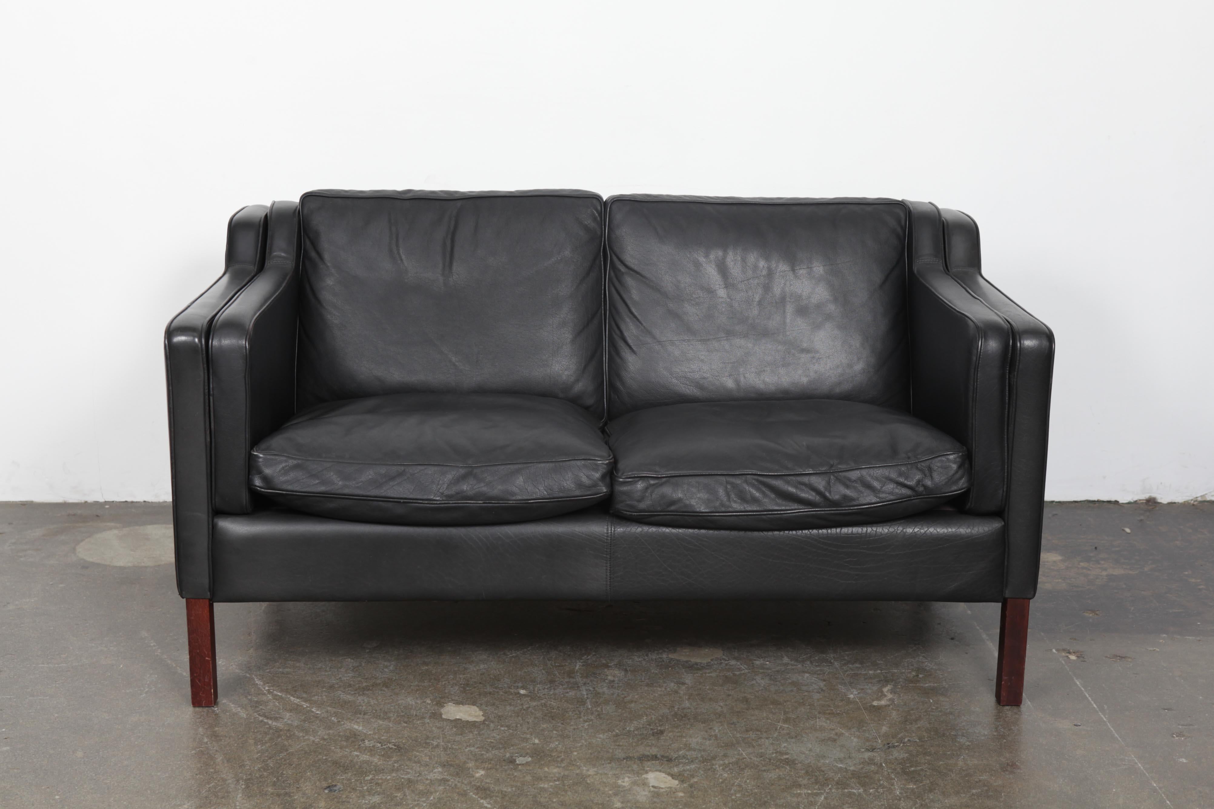 Two-seat sofa produced by reputable maker Stouby, Denmark, 1960s, in original black leather with rosewood legs. Shape and form are very much in the manner of Borge Mogensen. All leather in very good vintage condition with no tears or rips and very