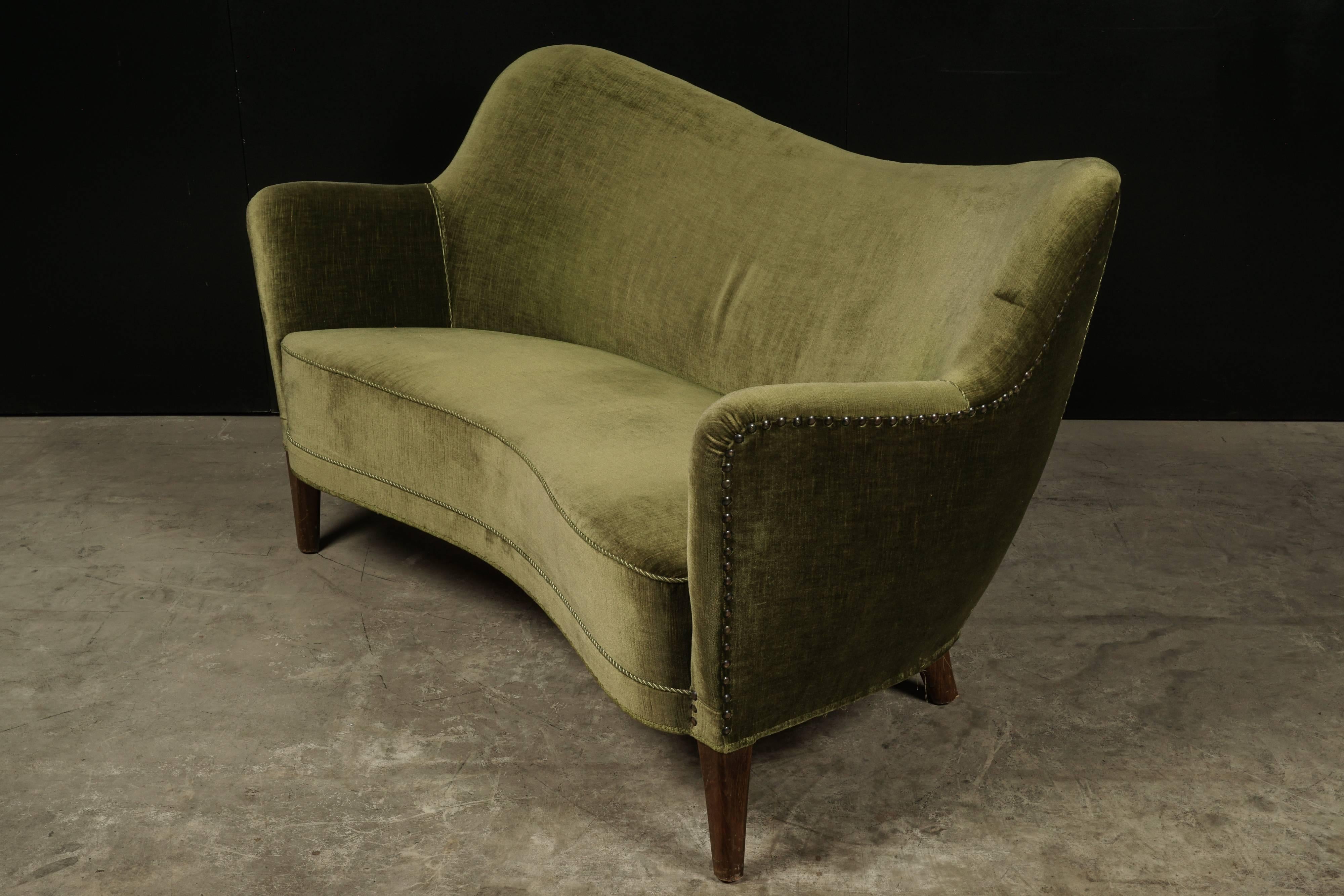 Midcentury two-seat sofa from Denmark, circa 1950. Banana form upholstered in green velour with feet of stained birch.