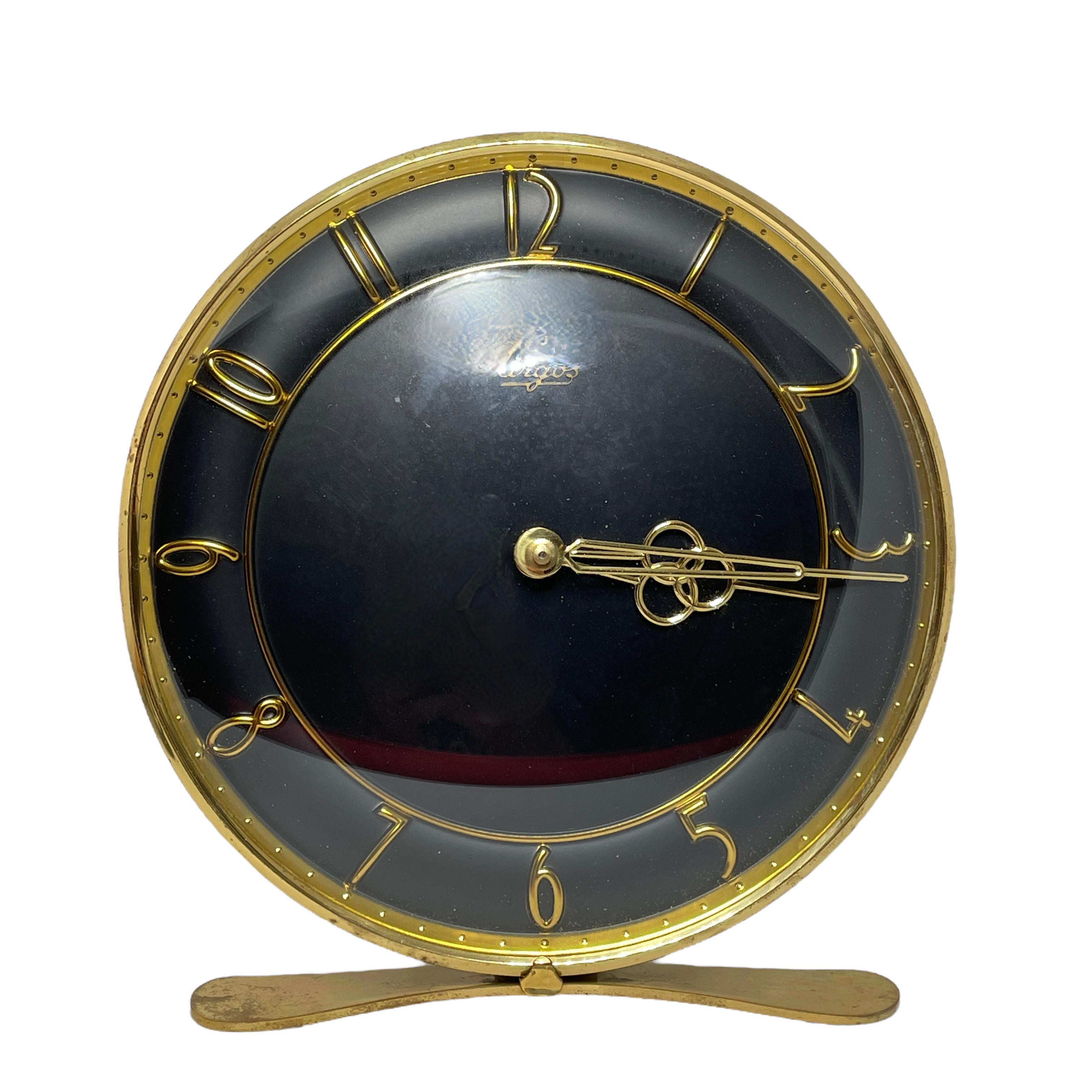 A beautiful Mid-Century Modern brass desk clock with a black clocks face. Executed in the 1950s by Urgos, Germany. Original movement in working condition. The brass with tarnished spots and patina, but this is old-age.