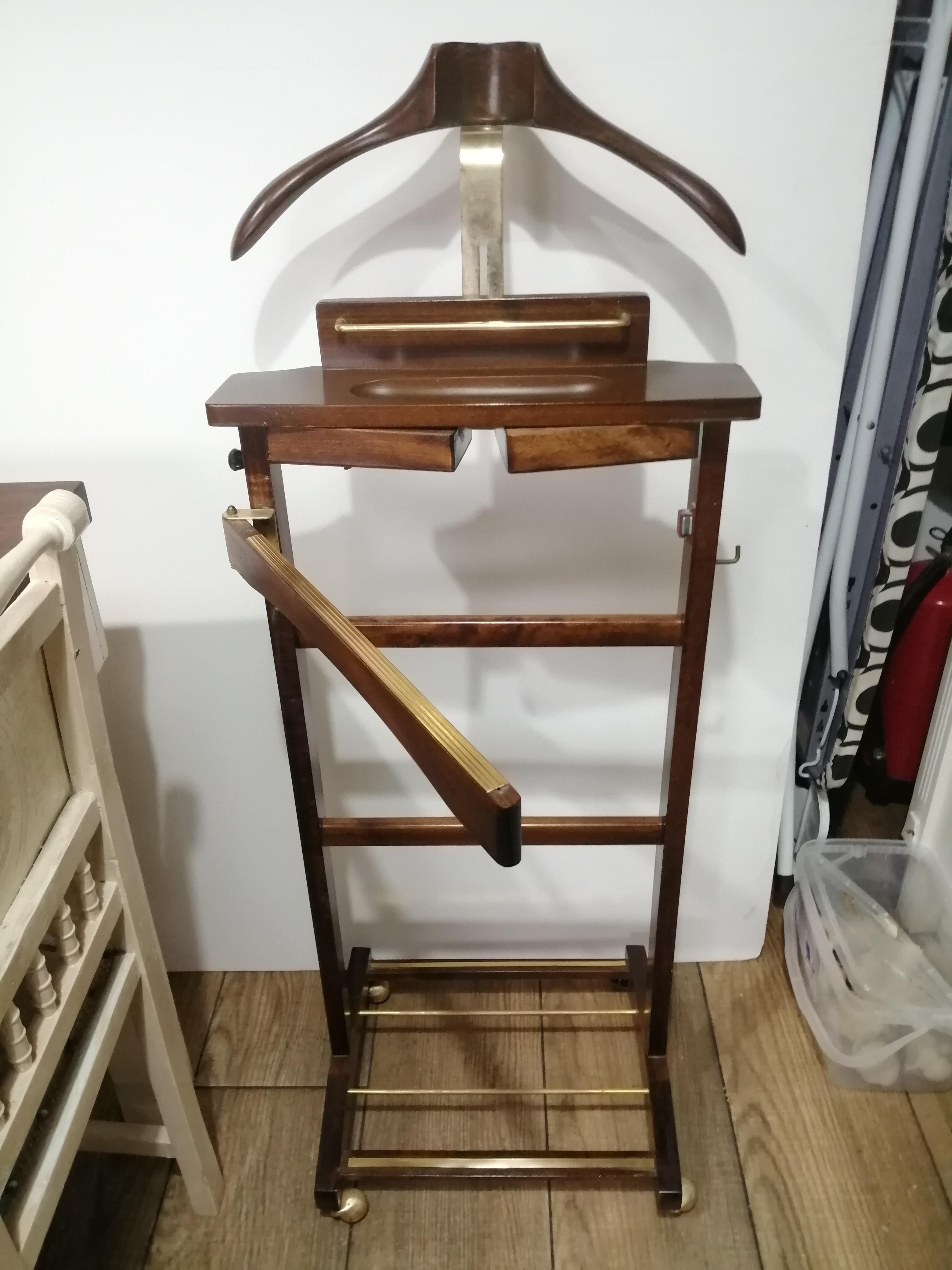 A 20th century Italian valet of wood brown color and brass, with drawers to introduce the twins or jewelry and bar to hang the pants

At the bottom it has a bar to put the shoes and on the sides a brush and a shoehorn

The jacket holder is